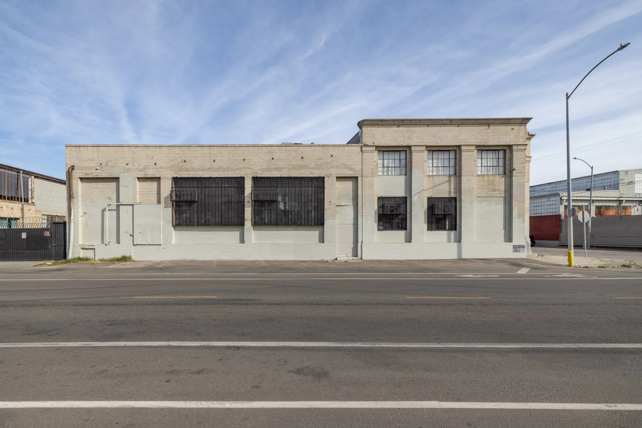 Empty building with barred windows on a city street, under a blue sky with light clouds.