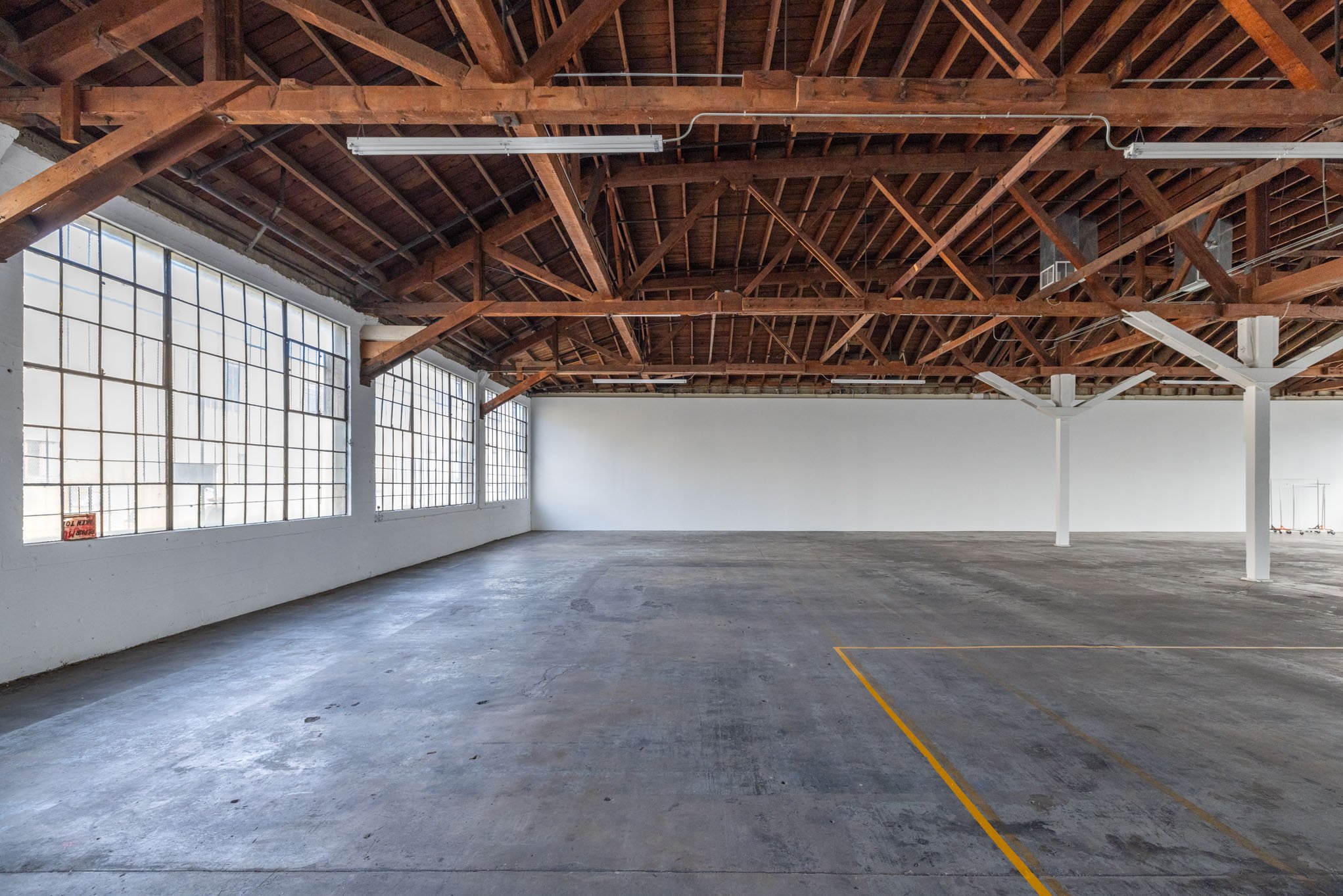 Empty industrial-style parking garage with large windows, exposed wooden beams, and concrete floor.