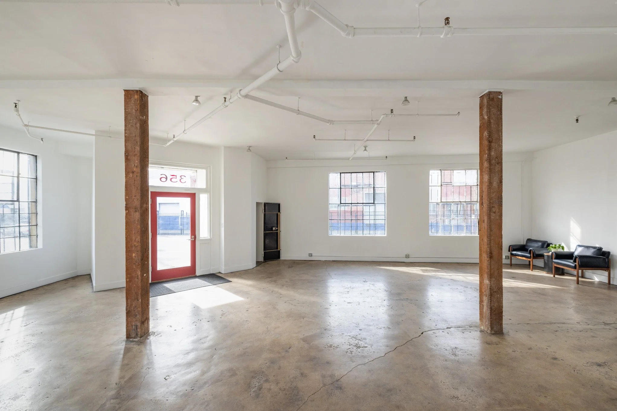 Empty commercial or gallery space with concrete floor, white walls, large windows, and two metal support columns.