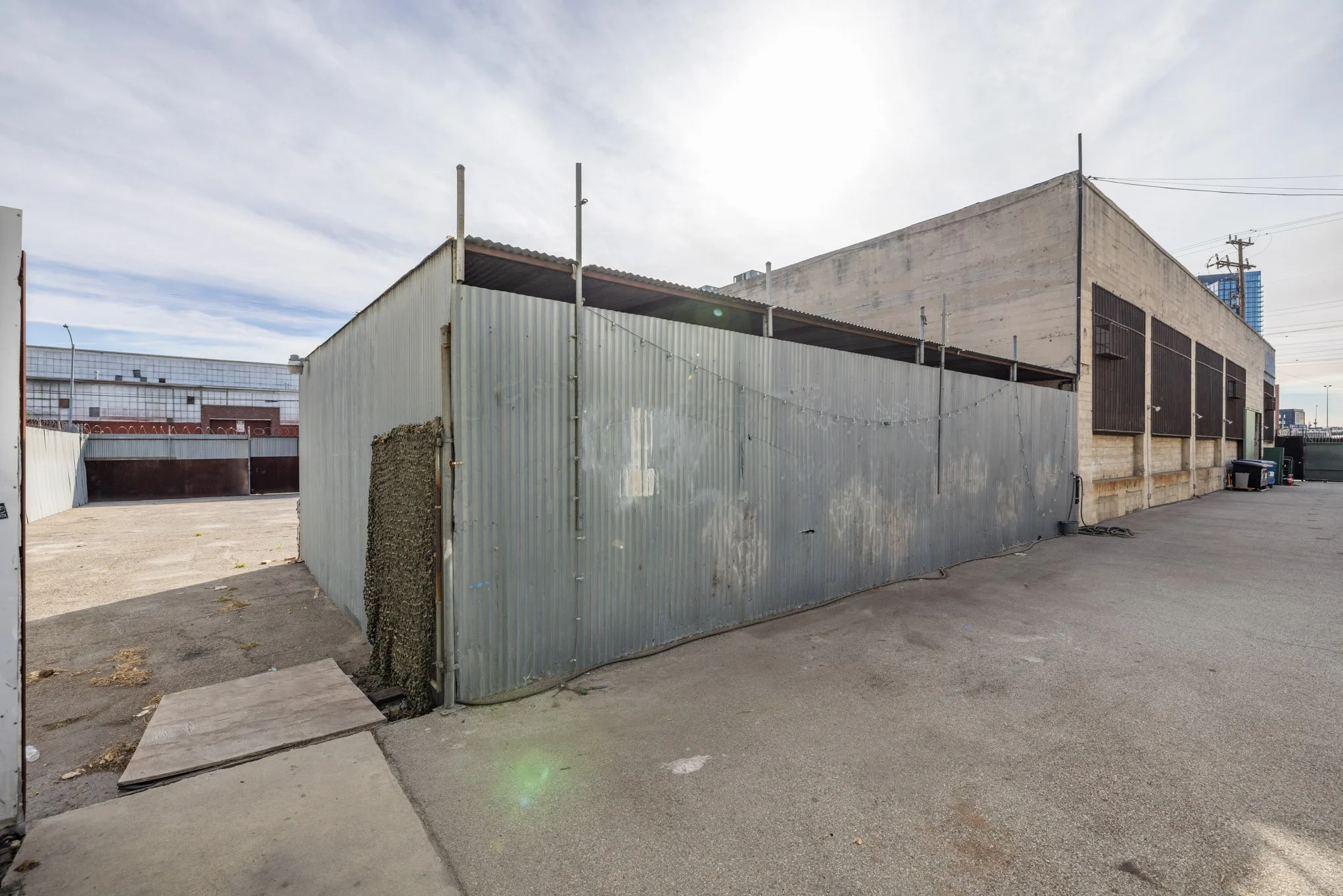 Empty outdoor parking lot with a metal fence and warehouse building under a cloudy sky.