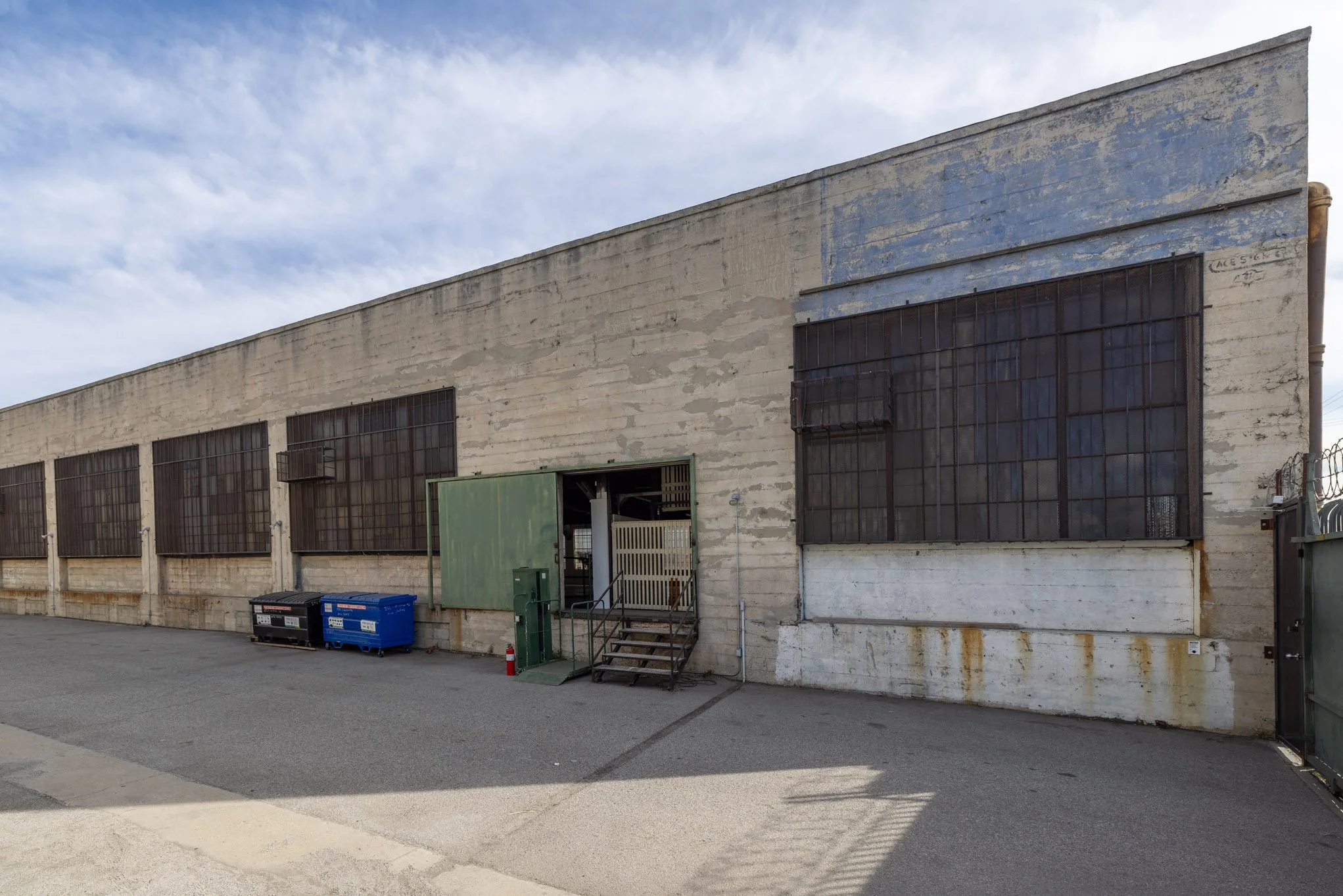 An old concrete building with large barred windows and a blue sky with scattered clouds.