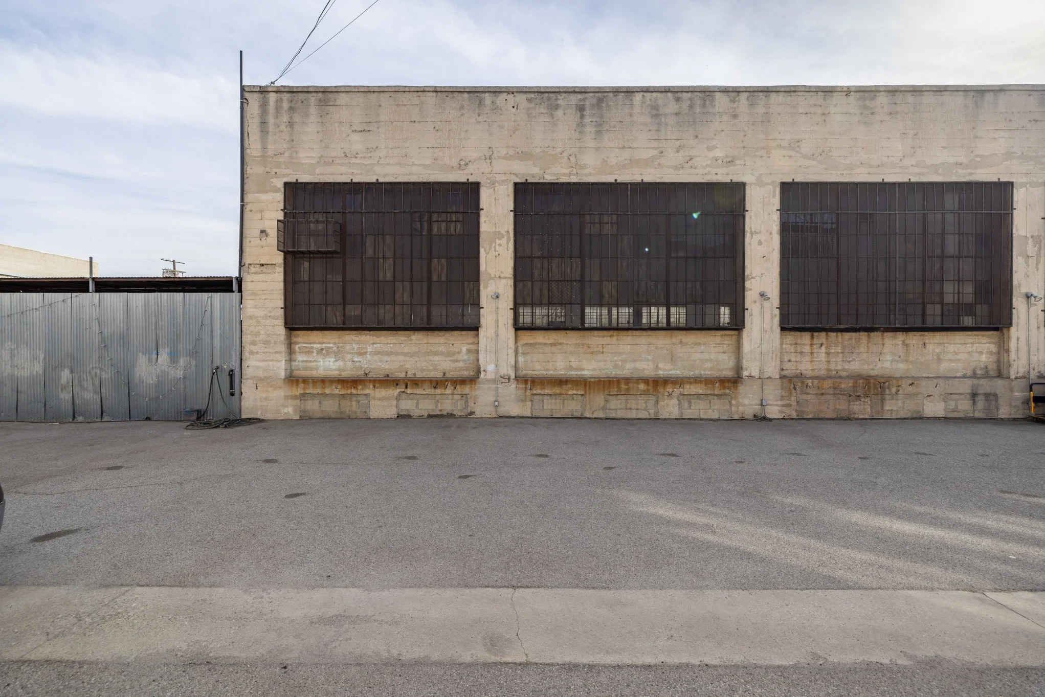 An old, weathered industrial building with barred windows, a metal side door, and a paved foreground.