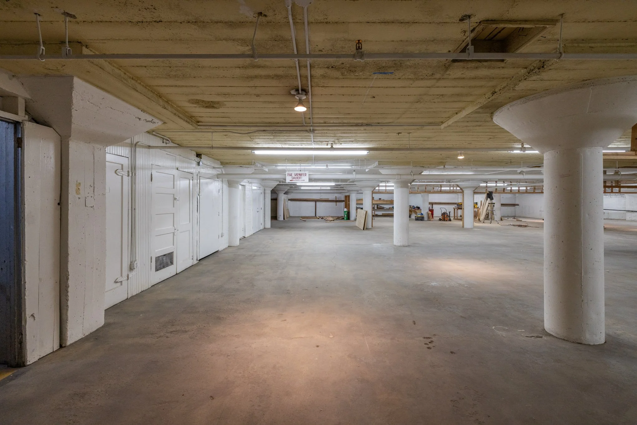 Empty indoor parking garage with white support columns, unfinished ceiling, and a concrete floor.