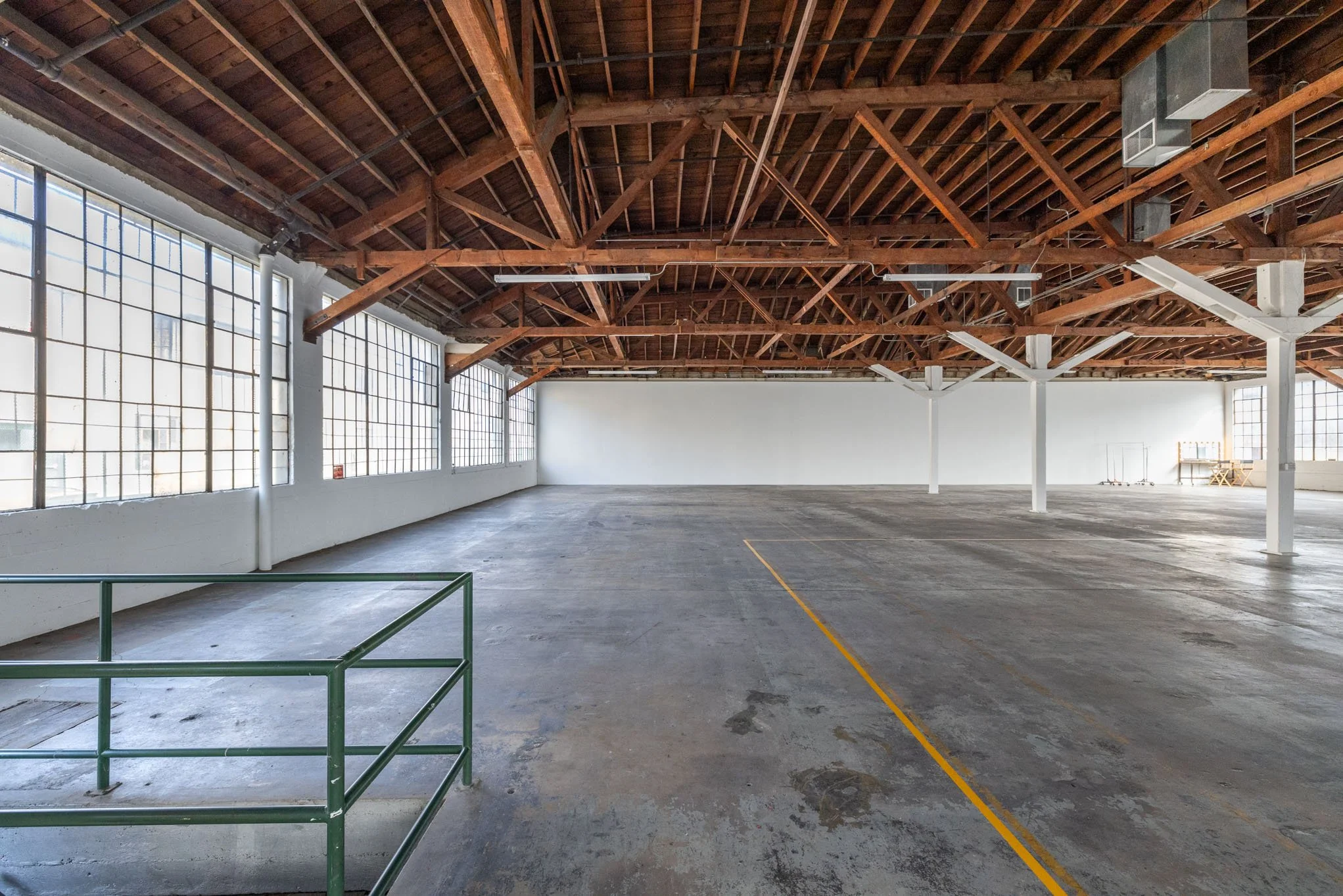 Empty indoor parking garage with concrete floor, wooden roof beams, large windows, and white walls.