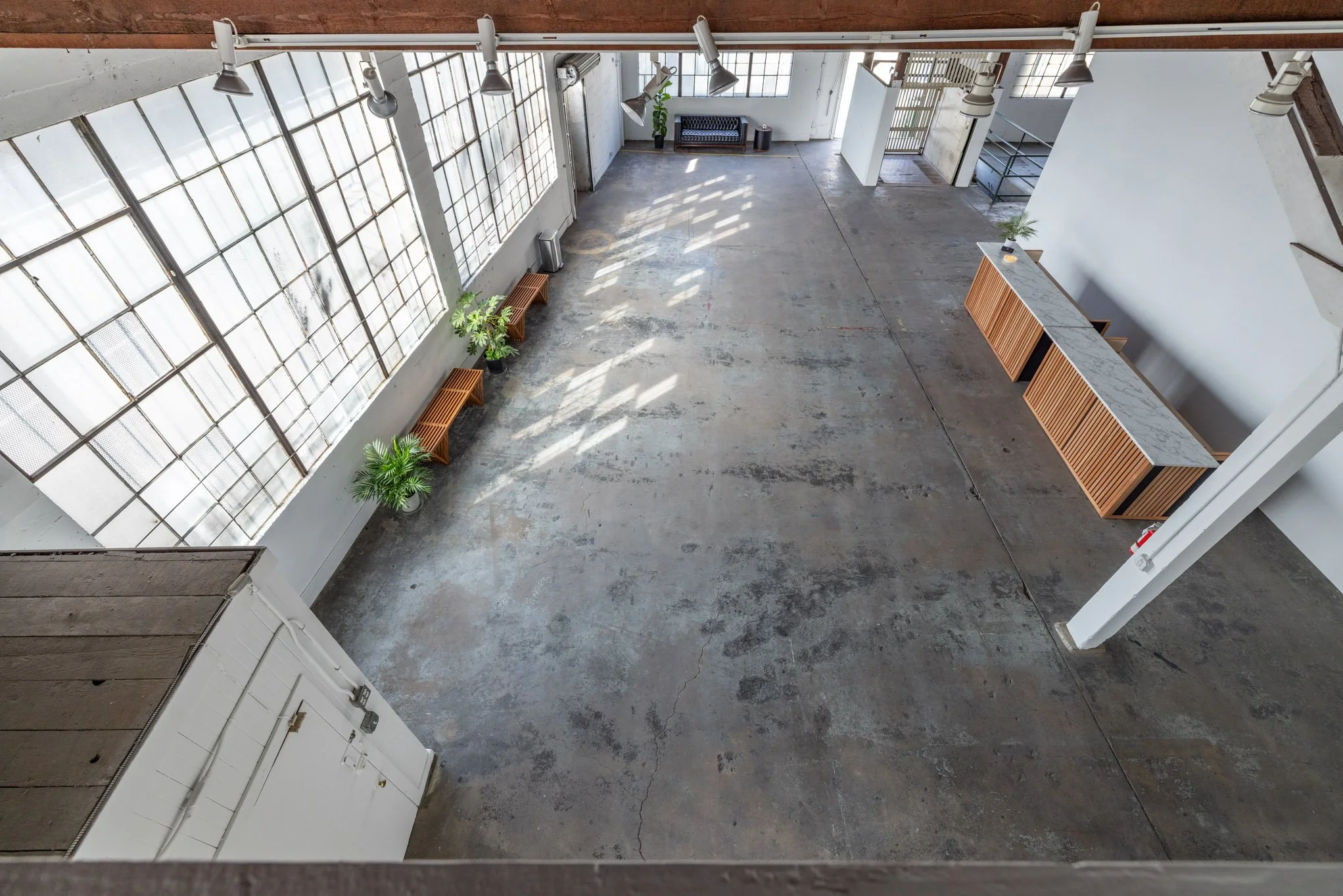 Empty industrial-style loft with large windows, concrete floor, potted plants, and modern furniture.