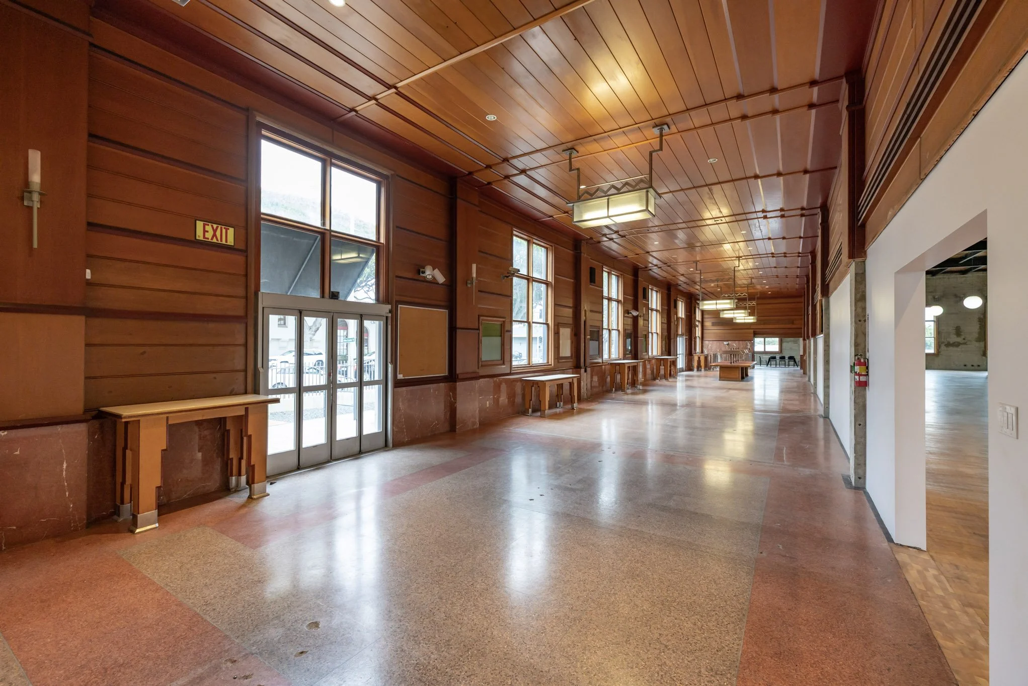 Empty lobby with wooden paneling, large windows, and a few tables along the wall.