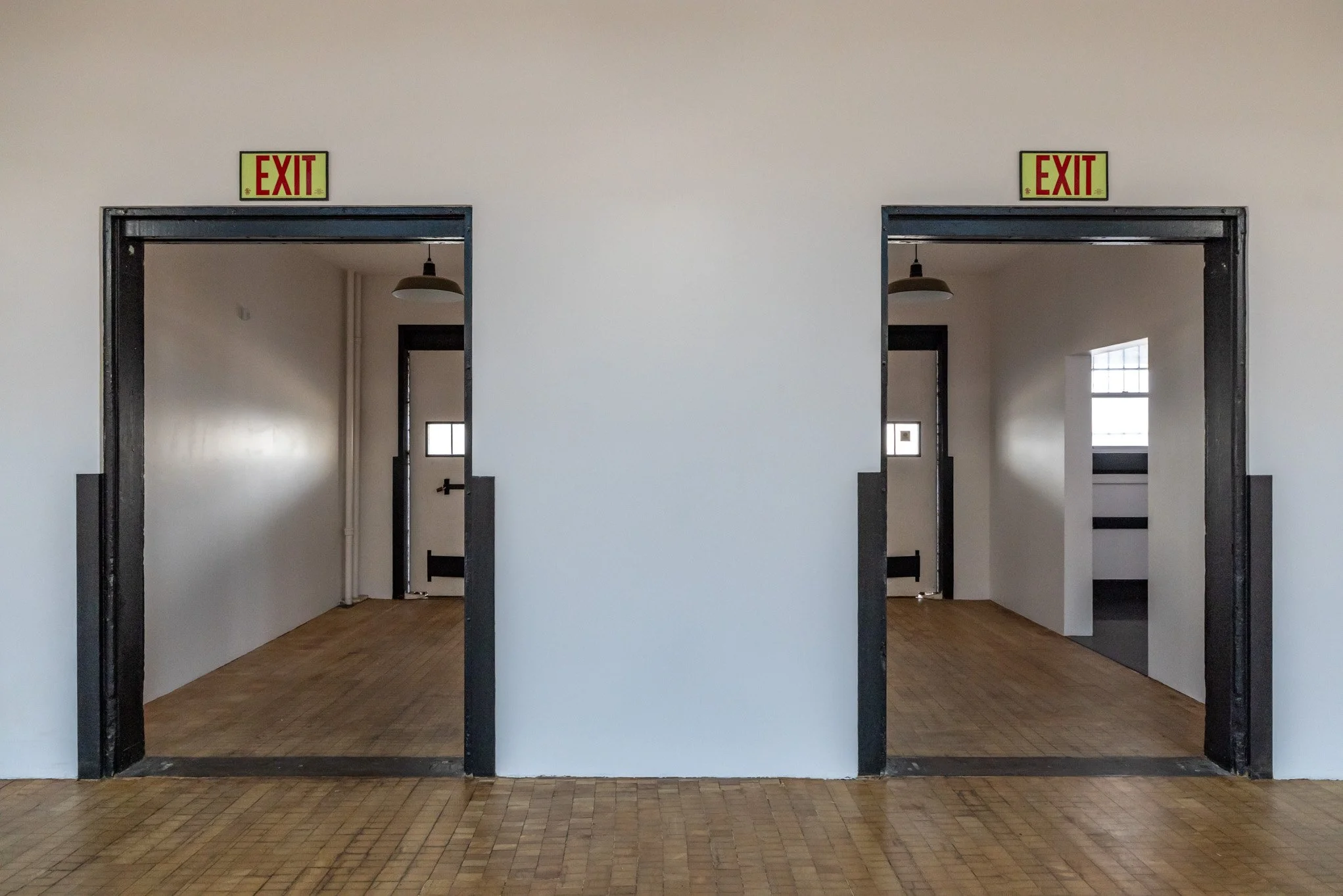 Two doorways labeled 'EXIT' in a white wall, with a view into small rooms with hardwood floors, small windows, and black framing.
