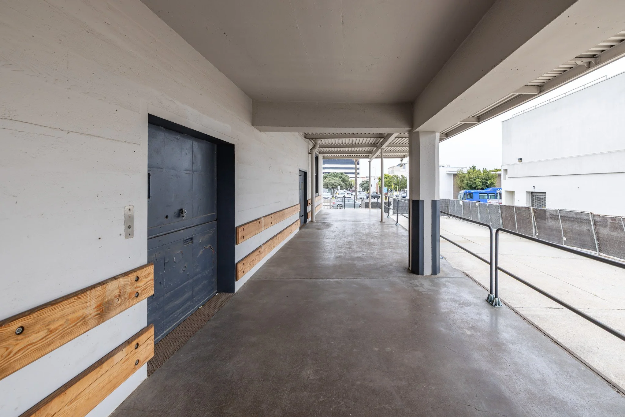 Empty outdoor hotel or apartment walkway with white walls, wood safety rails, and parking lot in the background.