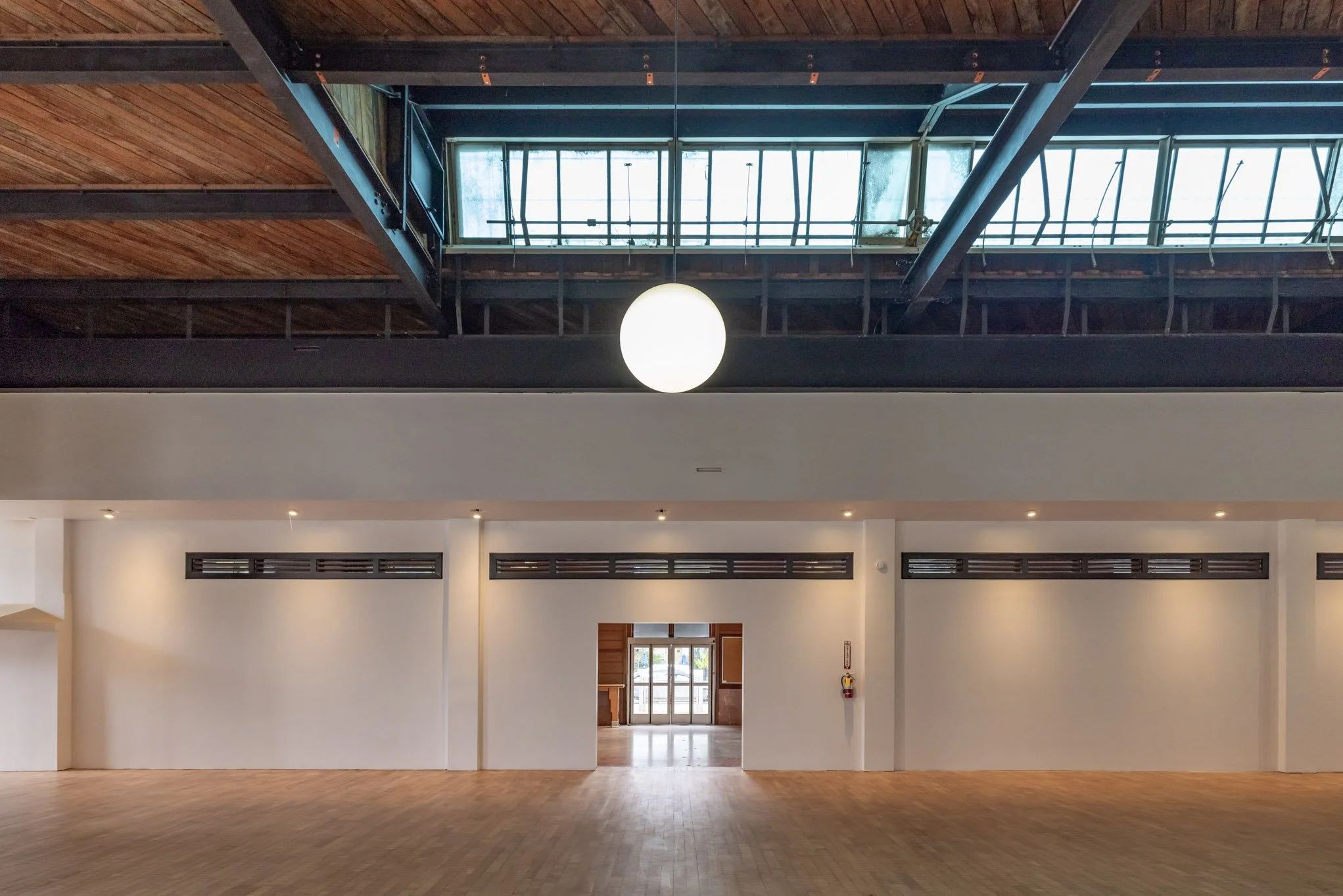 Large empty room with wooden floor, white walls, and a ceiling with a skylight and hanging light fixture.