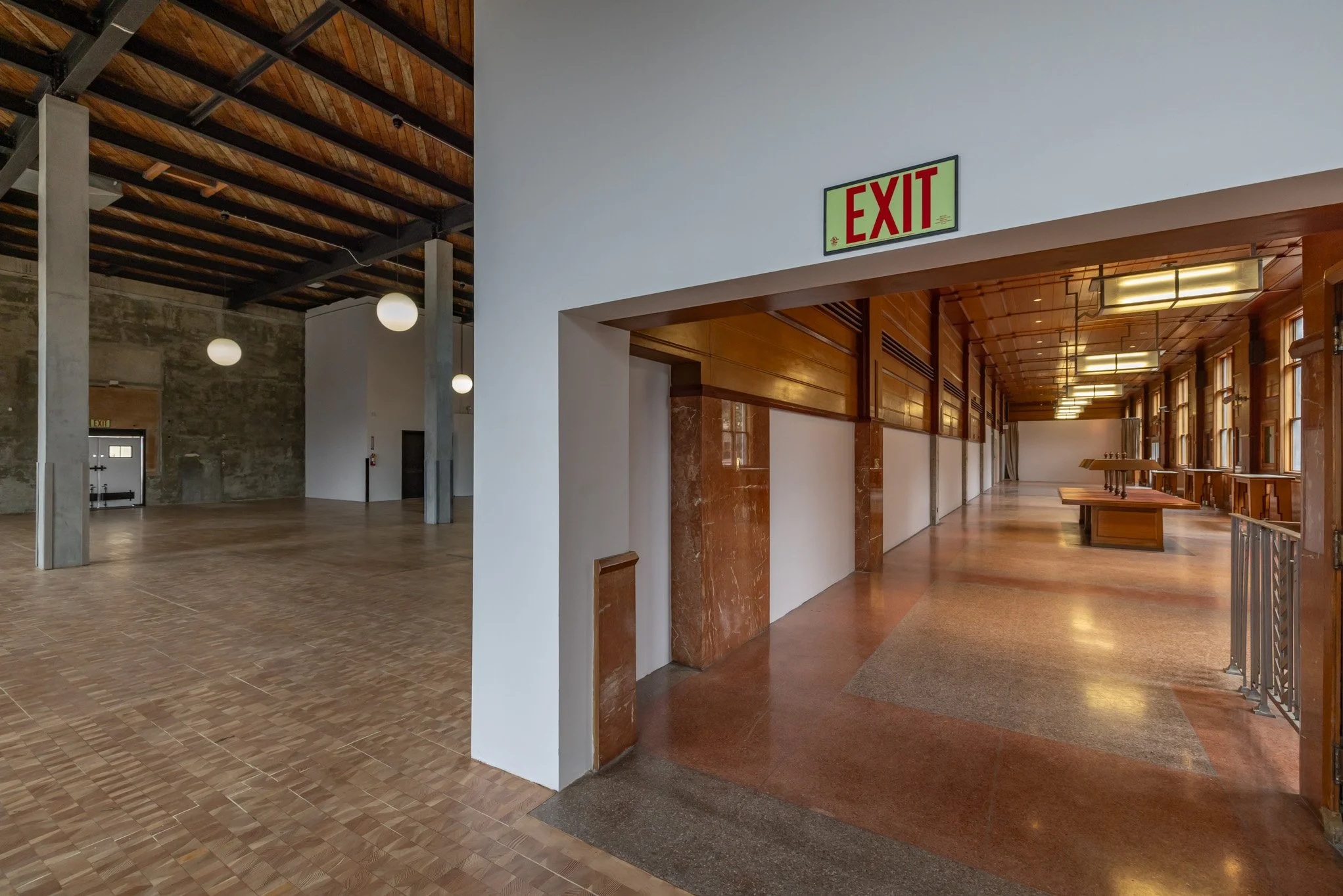 Interior view of a building with wooden ceiling and floors, featuring an exit sign above a corridor.