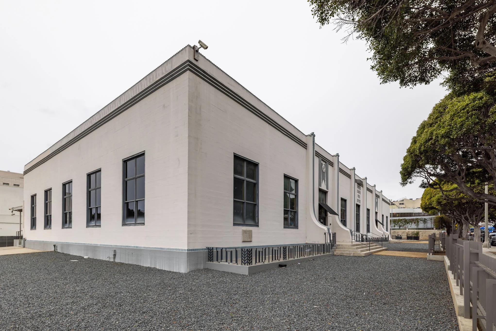 White historic building with multiple windows, stairs leading to entrance, and trees nearby