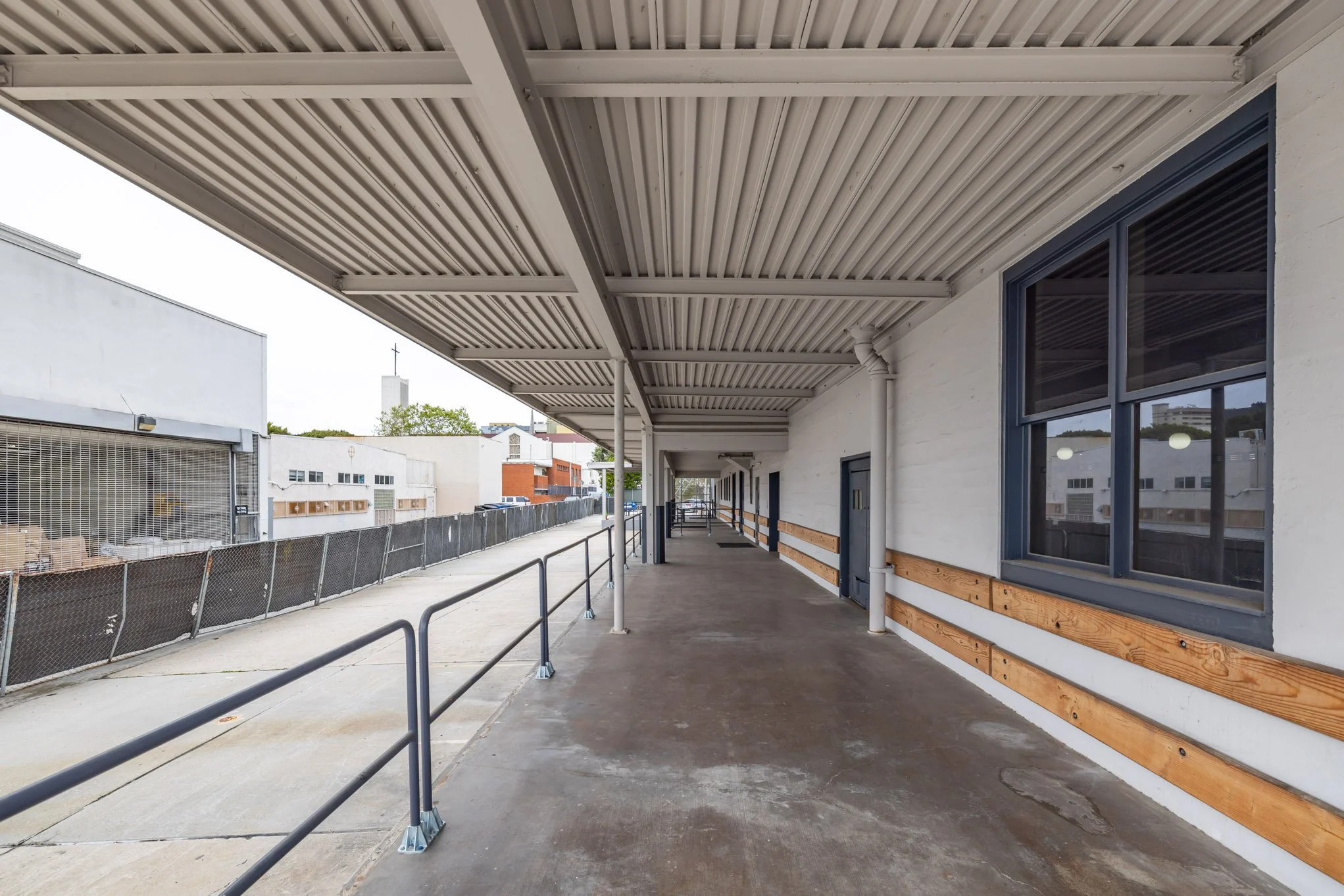 Empty outdoor sidewalk with a covered walkway, metal railing, and building with windows and wood accents, in an urban area.