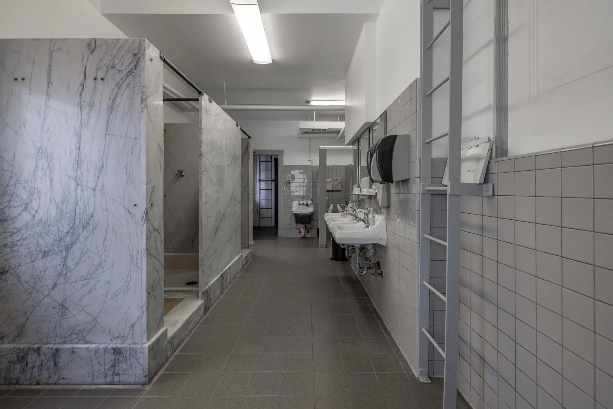 Public men's restroom with sinks, a soap dispenser, and shower stalls with marble partitions.