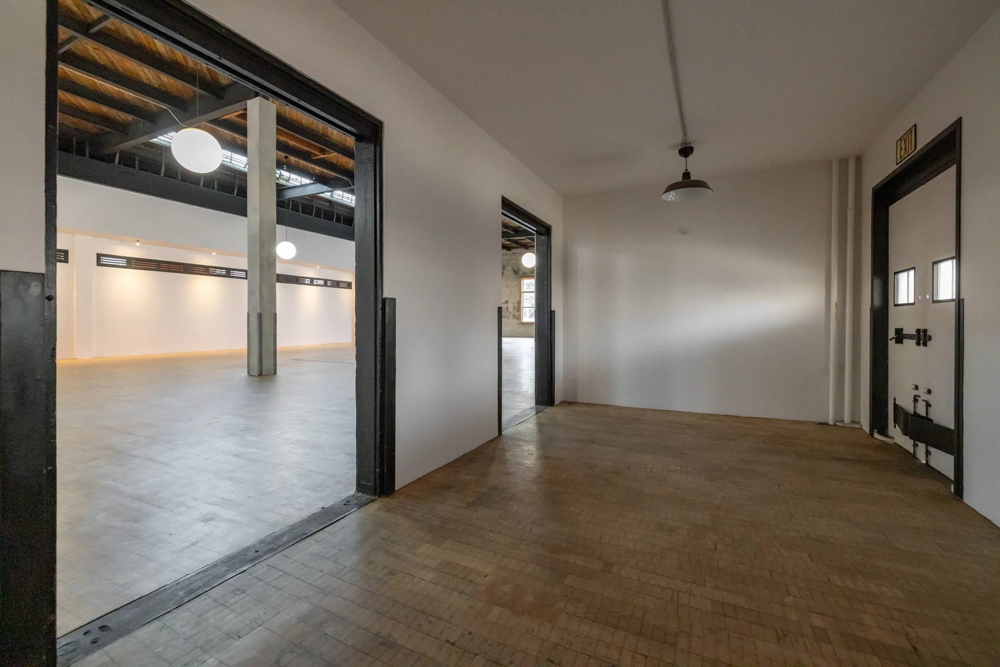 Empty interior space with wooden floors, white walls, and doorway openings leading to other rooms, with modern industrial design elements.