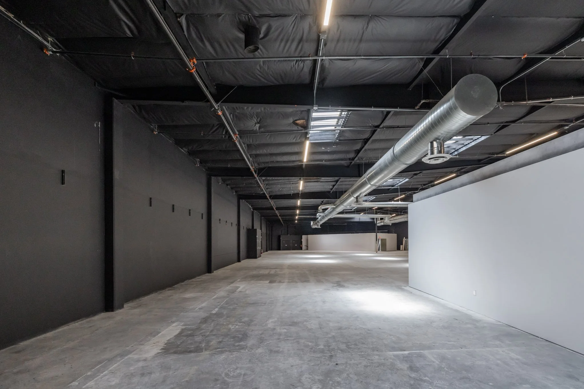 Empty interior space with black and white walls, exposed ceiling with ductwork, and concrete floor.