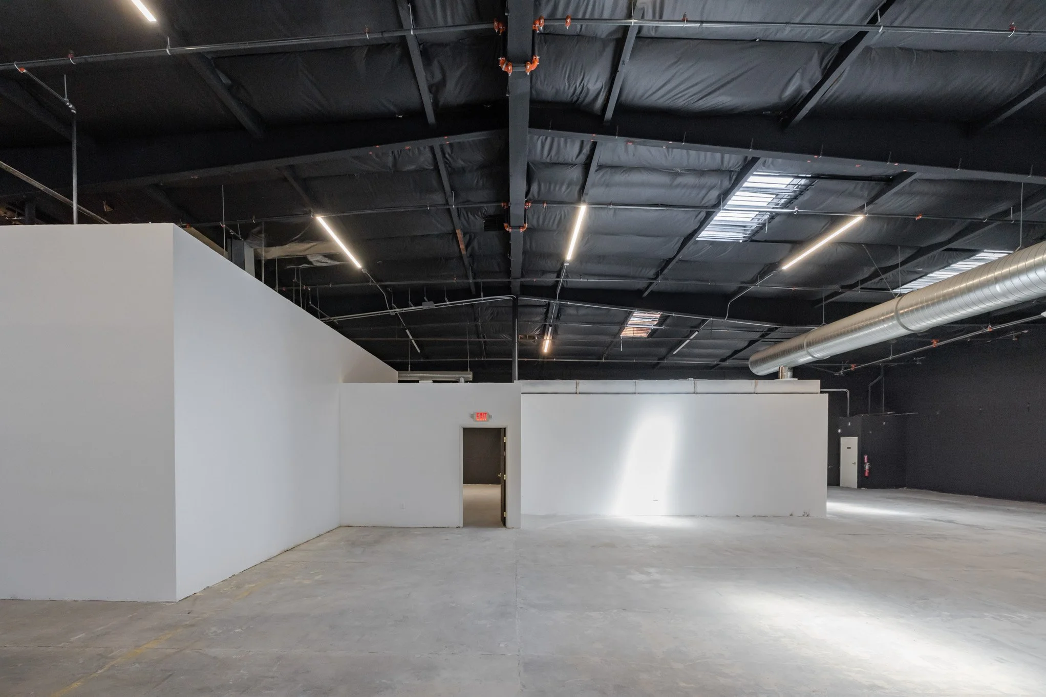 Empty commercial or industrial interior space with white walls, a black ceiling with exposed ductwork, and concrete floor.