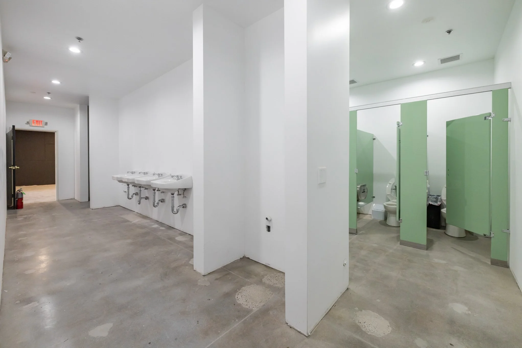 Public restroom with three sinks on the left, and three toilet stalls on the right with green partition doors.