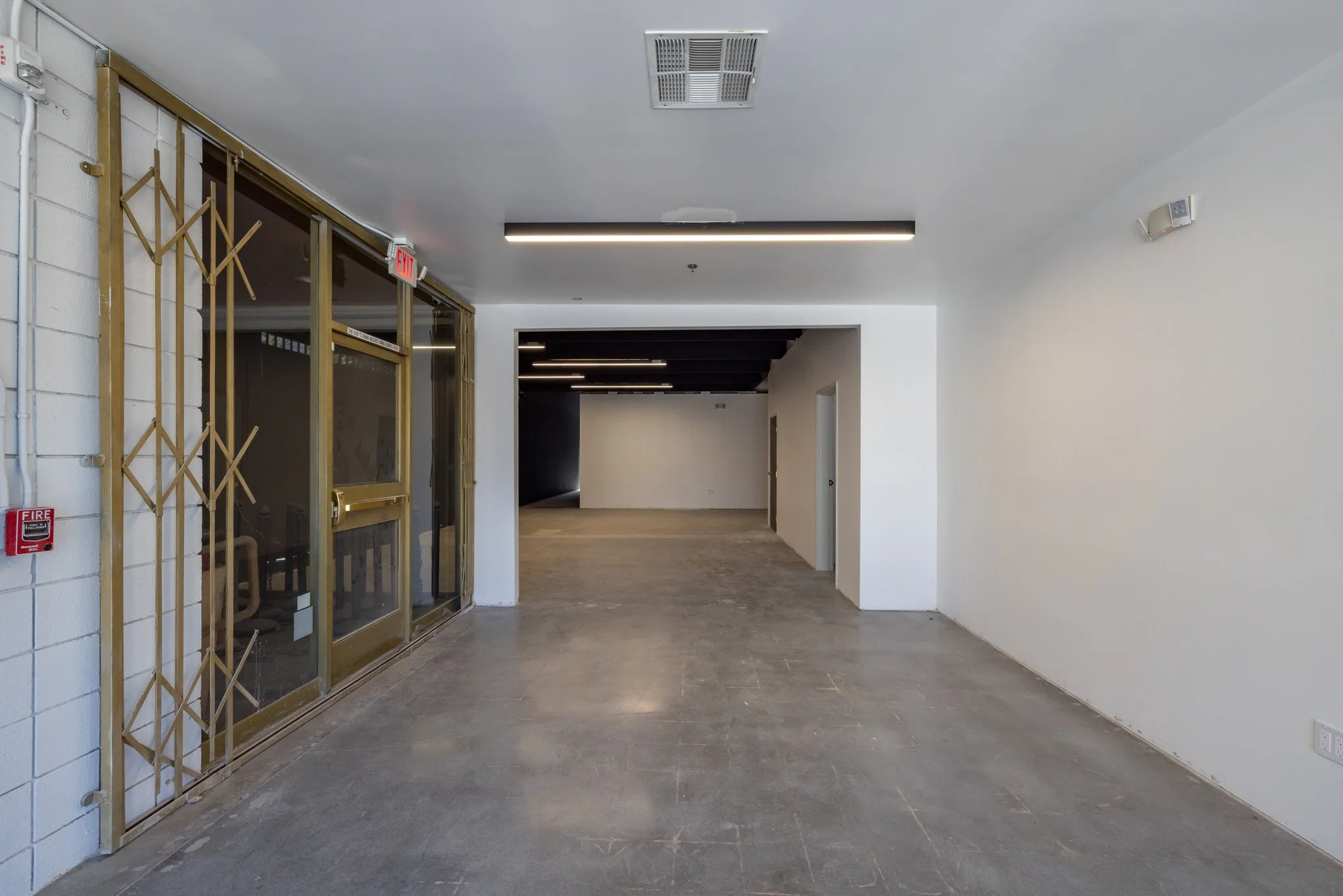 Empty commercial interior with a glass door entrance, white and black walls, ceiling ventilation, and unfinished flooring.