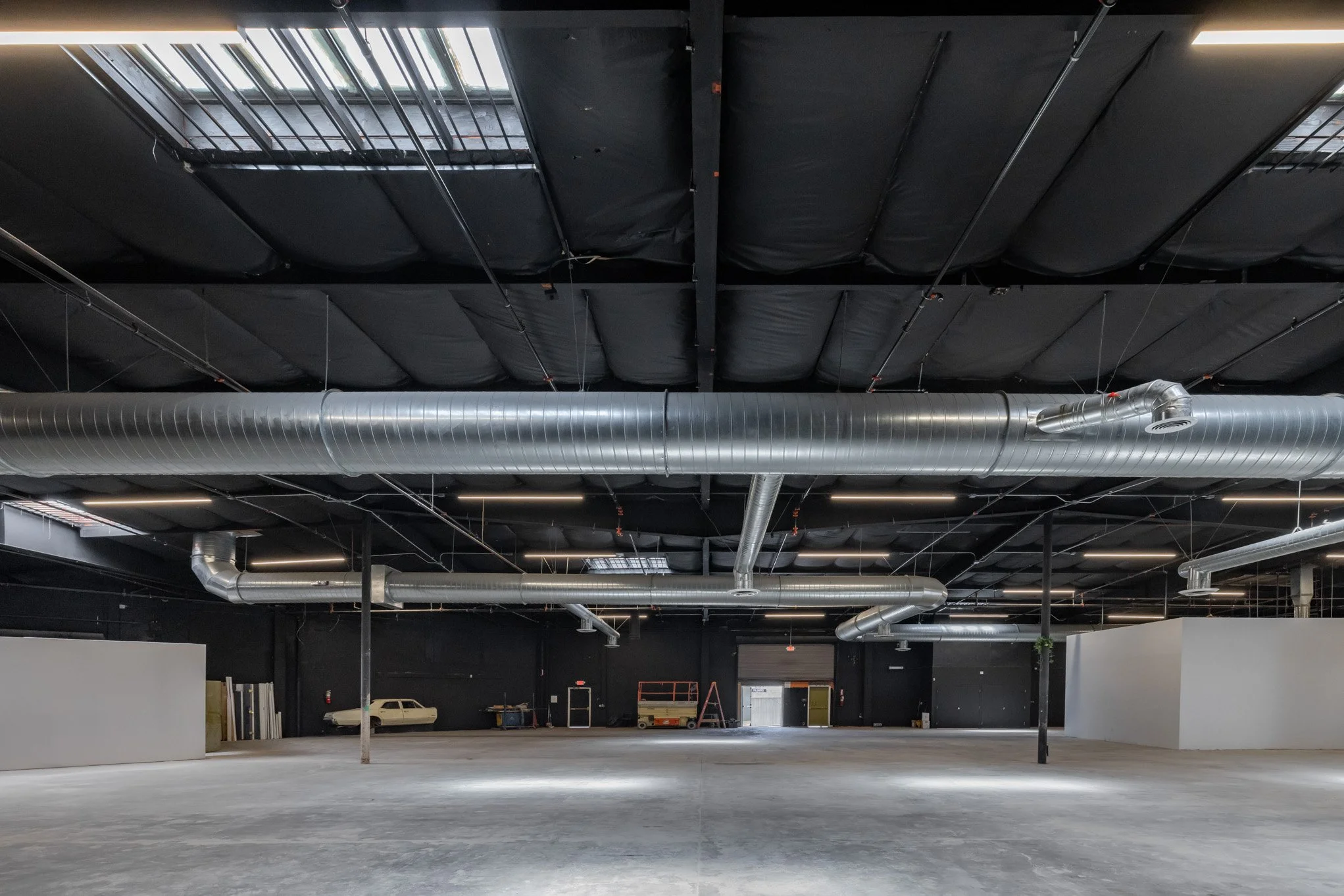 Empty commercial or industrial space with exposed ductwork, black ceiling, gray flooring, and minimal furnishings.