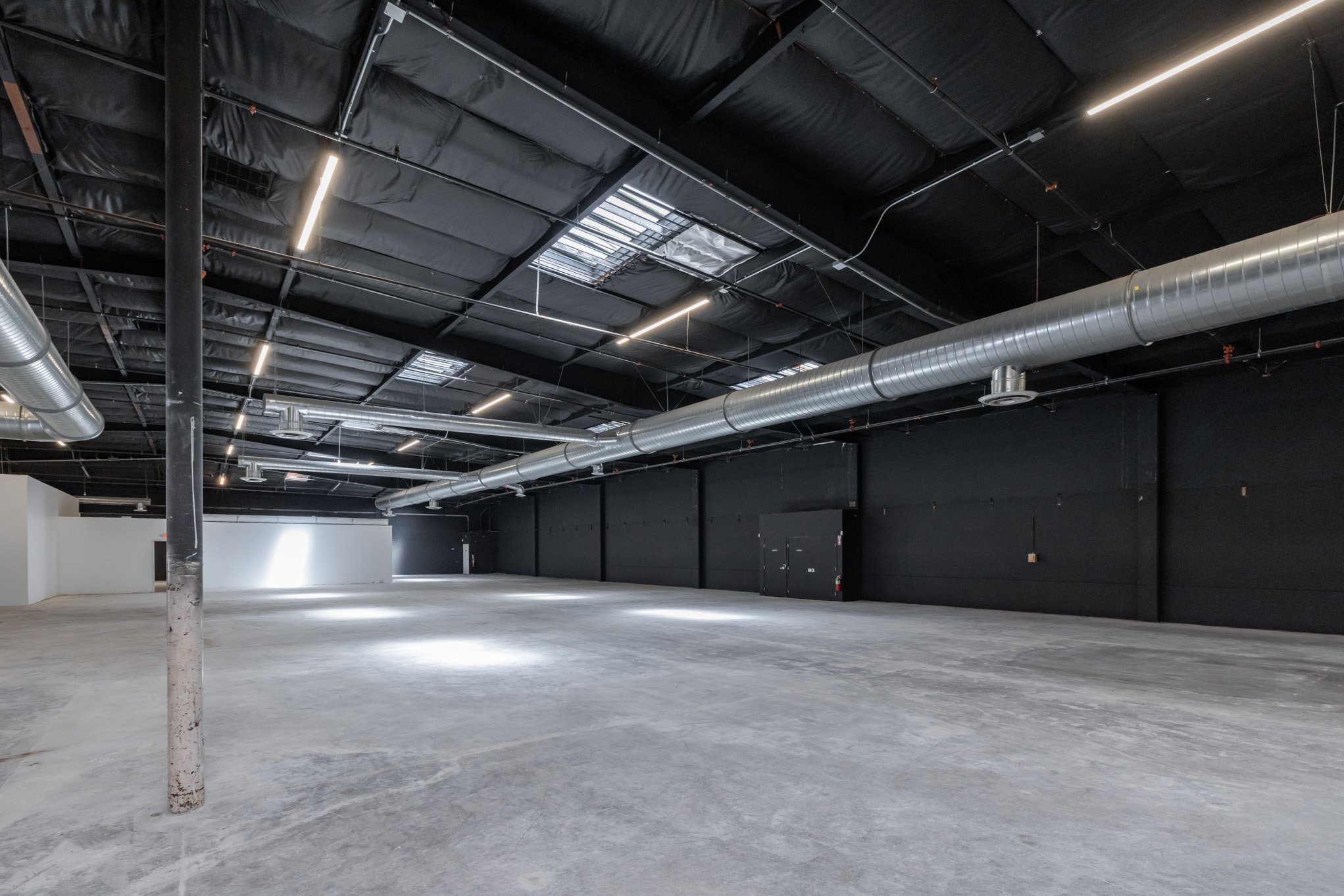 Empty industrial warehouse with black walls, metallic ventilation ducts, and LED strip lighting.