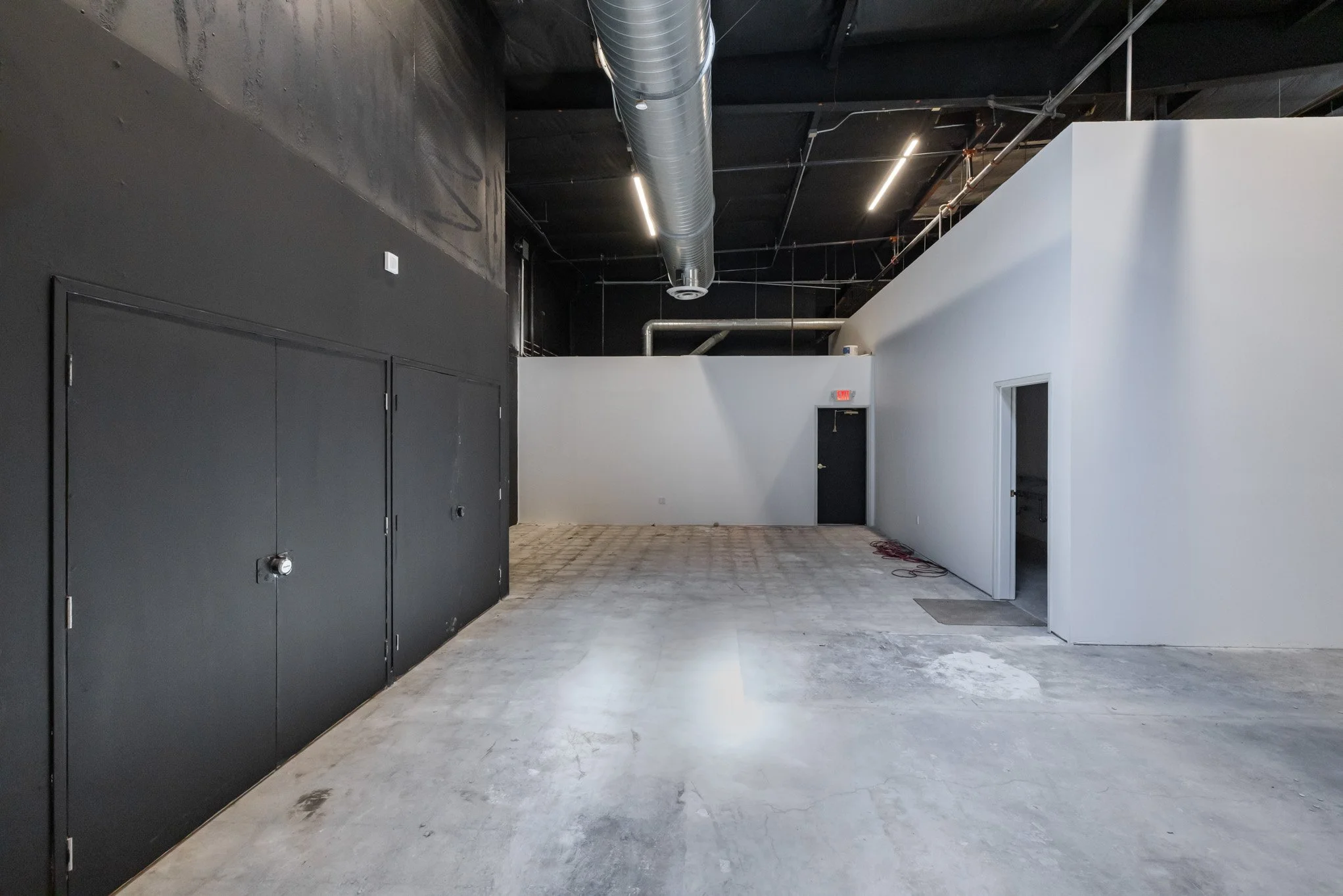 Interior of an unfinished commercial space with black and white walls, exposed black ceiling with ductwork, and concrete floor.