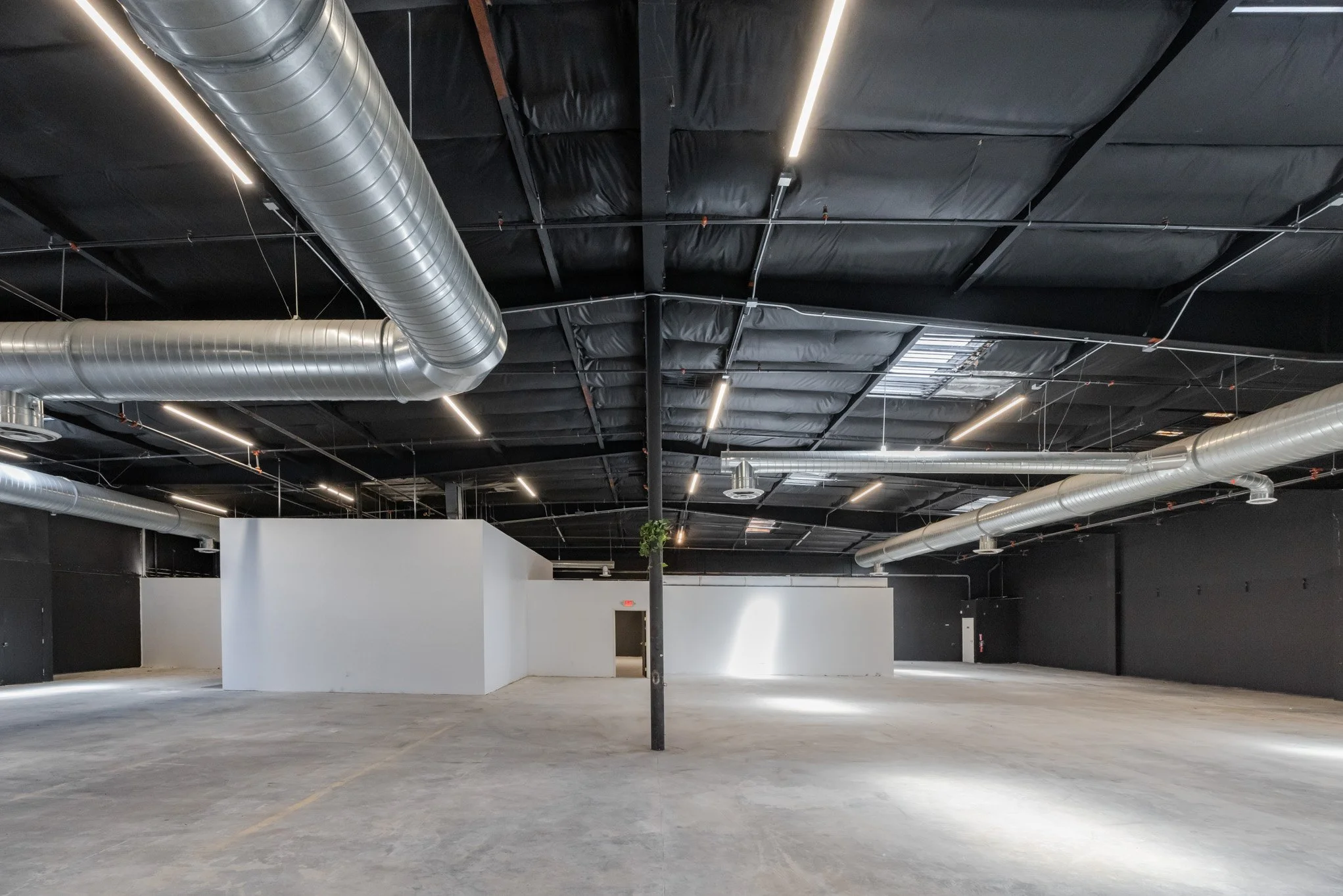 Empty industrial or commercial space with black ceiling, exposed ducts, and white walls.