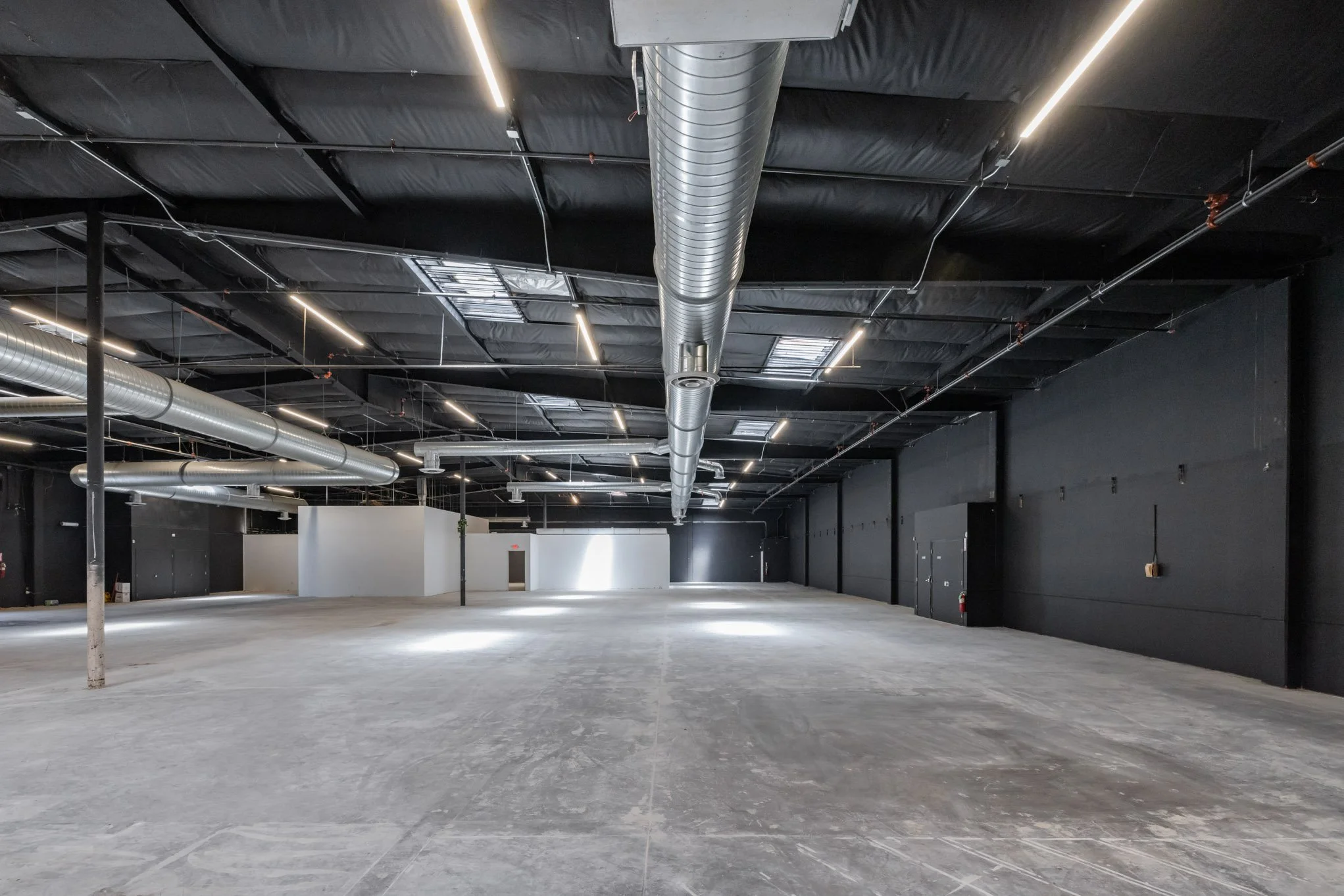 Empty industrial or commercial space with black walls, a black ceiling with exposed ductwork, and a concrete floor.