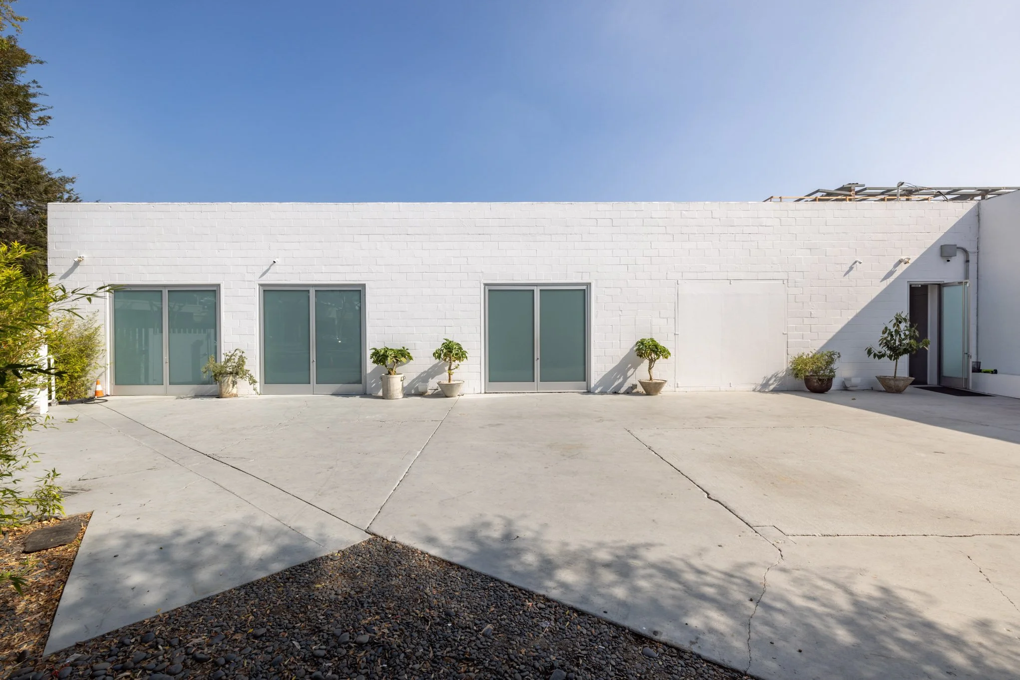 White modern building with large sliding glass doors, potted plants, and a concrete patio under clear blue sky.