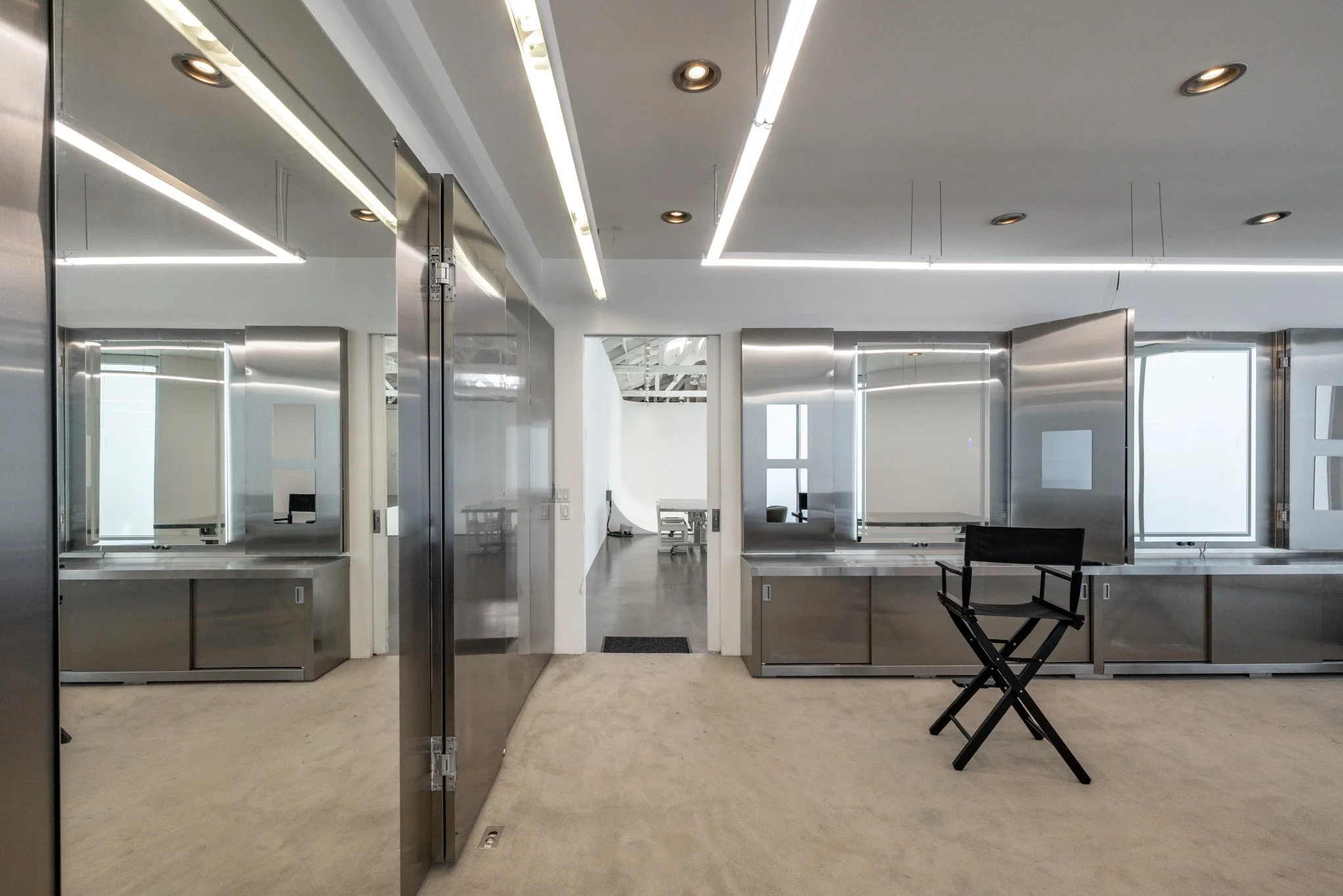 Modern, minimalistic office space with stainless steel serving counters, a black director's chair, and bright lighting.