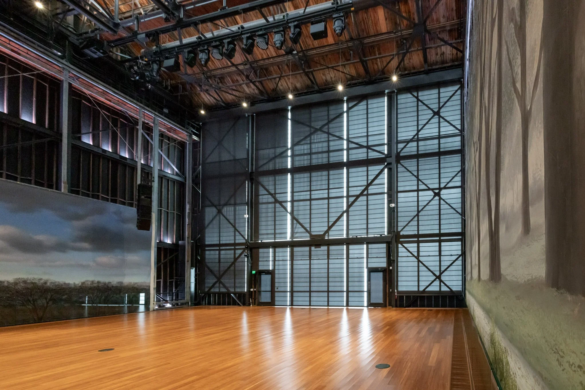 Empty art gallery with wooden flooring, large painting of a landscape on the right wall, and industrial-style metal and wood walls and ceiling
