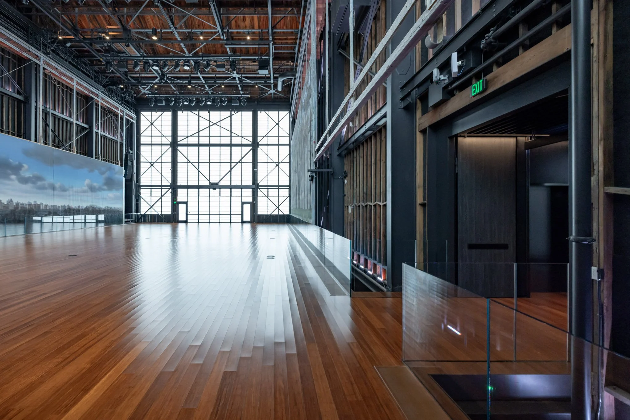 Empty interior space with wooden flooring, large windows at the far end, and a high ceiling with exposed structural beams.