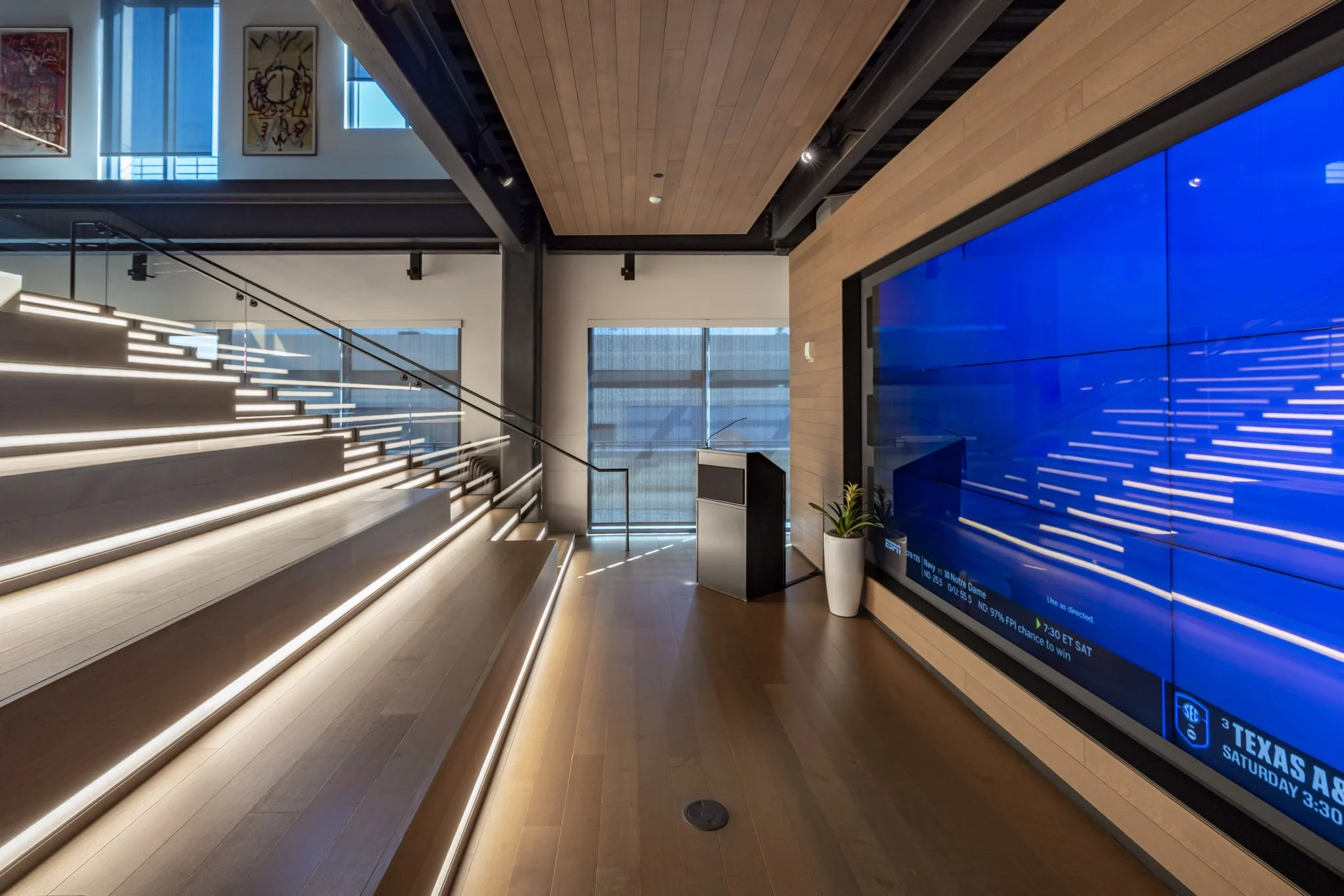 Modern interior with illuminated staircase, large flat-screen display, potted plant, and wood-paneled walls.