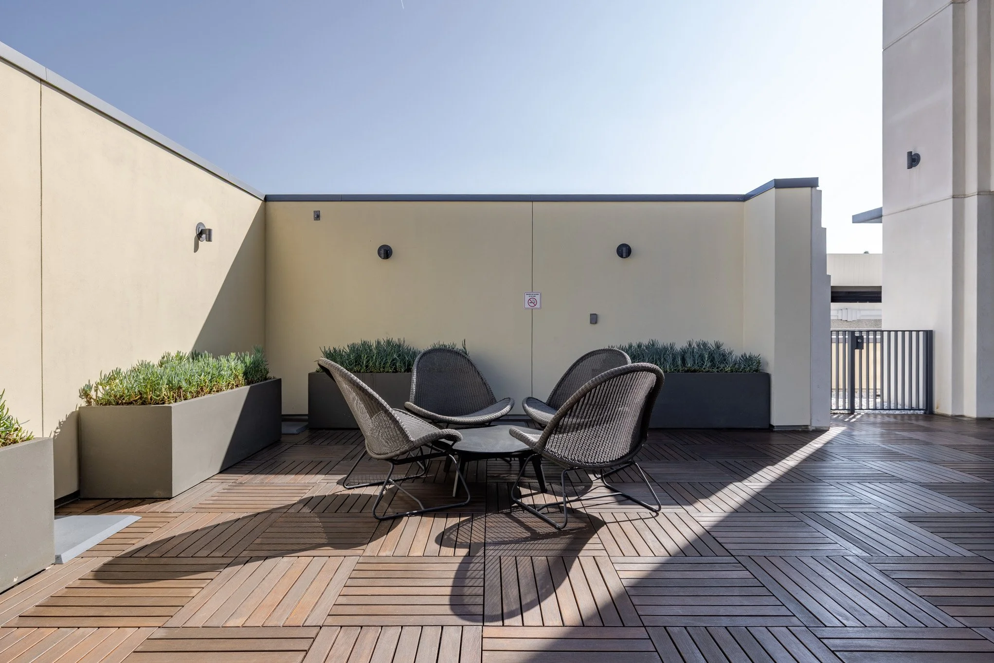 Rooftop patio with patio furniture, potted plants, and a no-smoking sign on a beige wall.