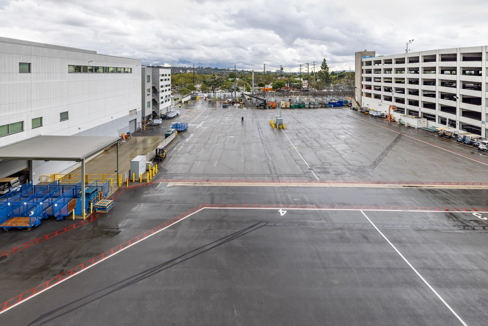 Empty parking garage with wet pavement, blue carts, storage areas, and overcast sky.