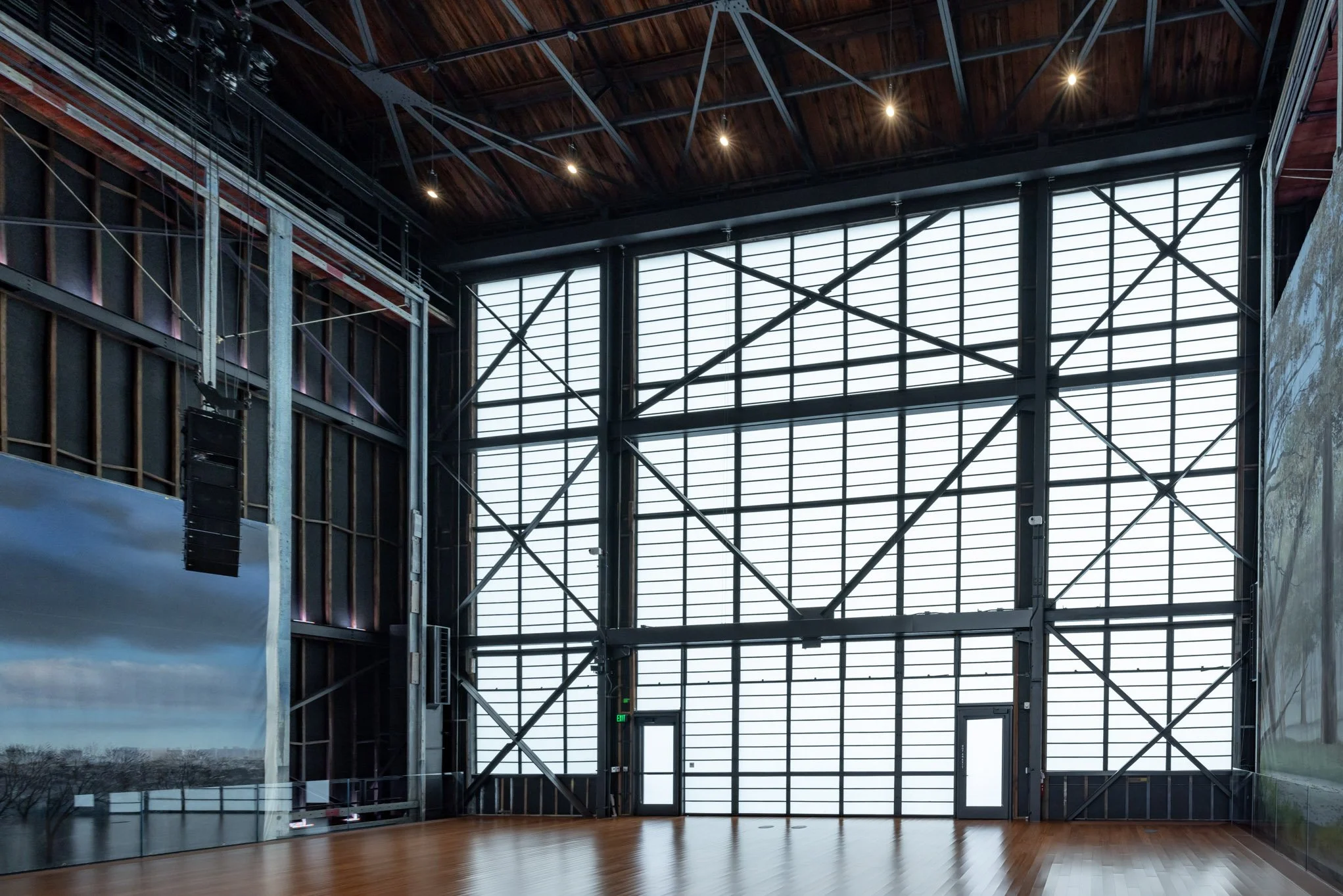 Interior of an industrial-style building with large windows, exposed steel framework, and wooden floors.