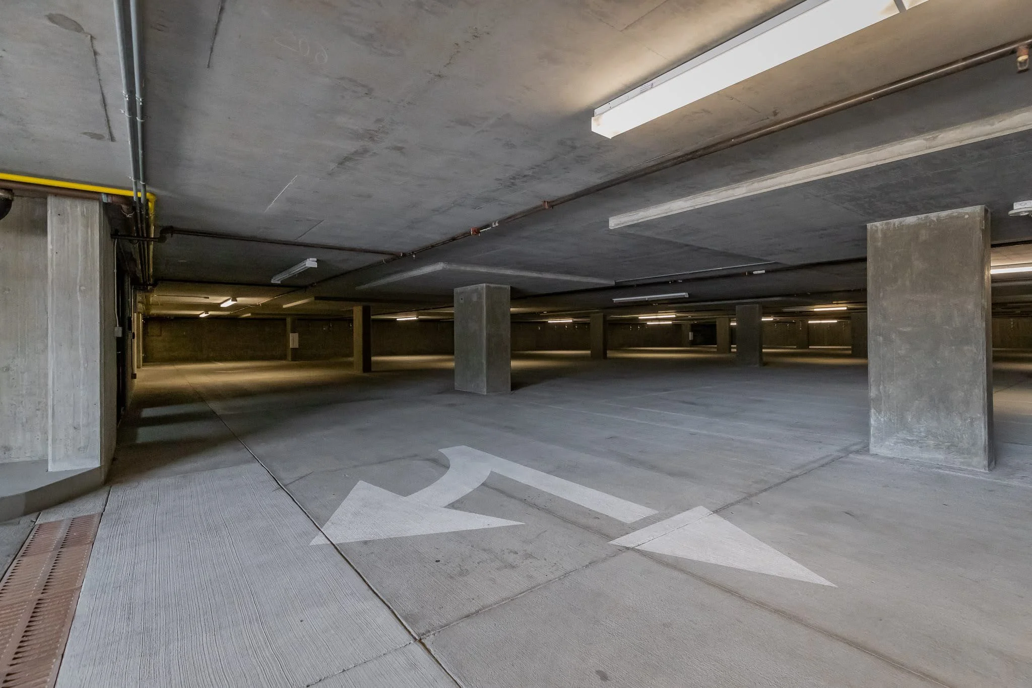 Underground parking garage with concrete pillars and a white arrow painted on the ground indicating a left turn.