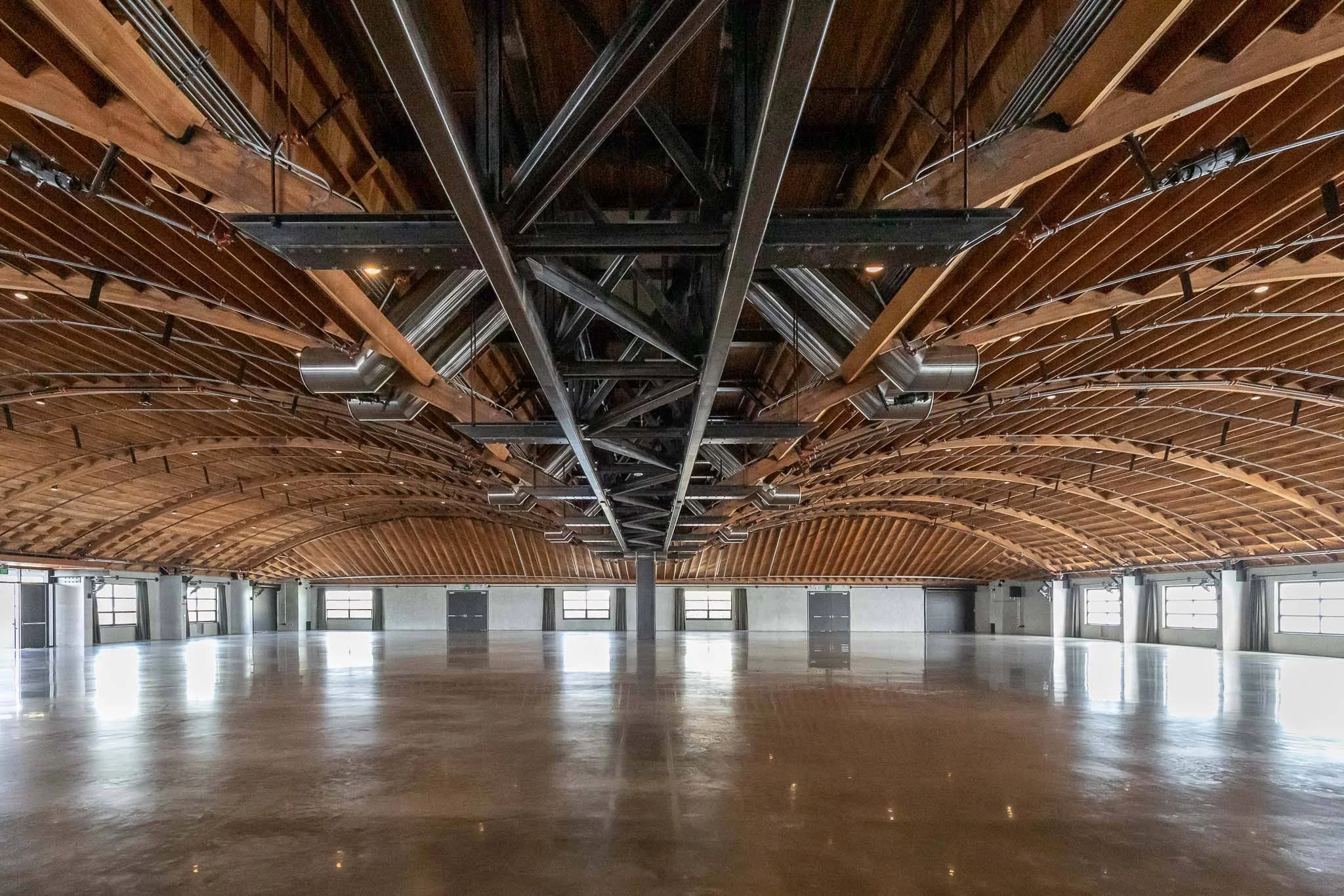 Empty indoor space with polished concrete floor, wooden arched ceiling, and multiple windows along the side walls.
