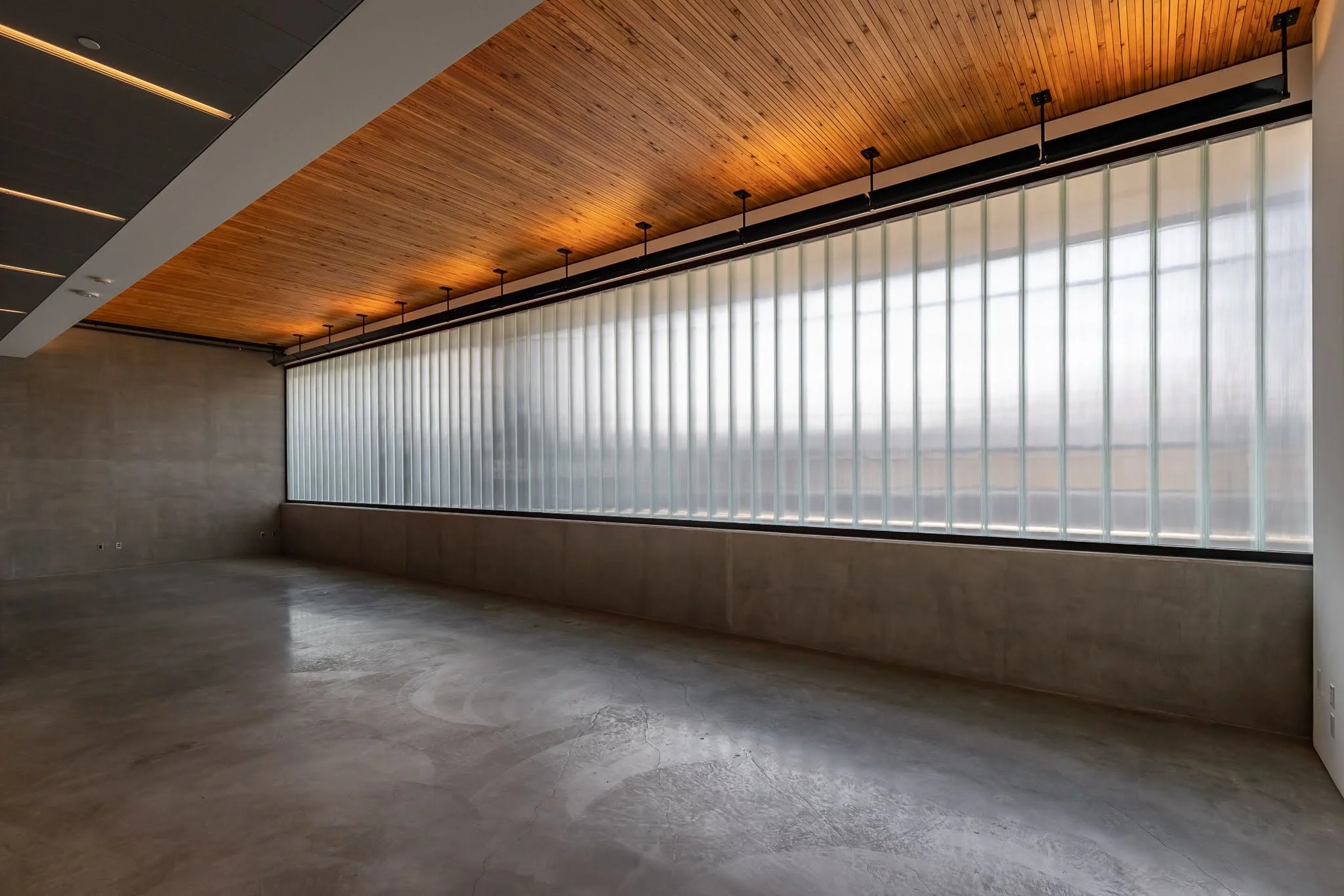 Empty modern room with large frosted window, concrete floor, wood ceiling, and minimal decor.