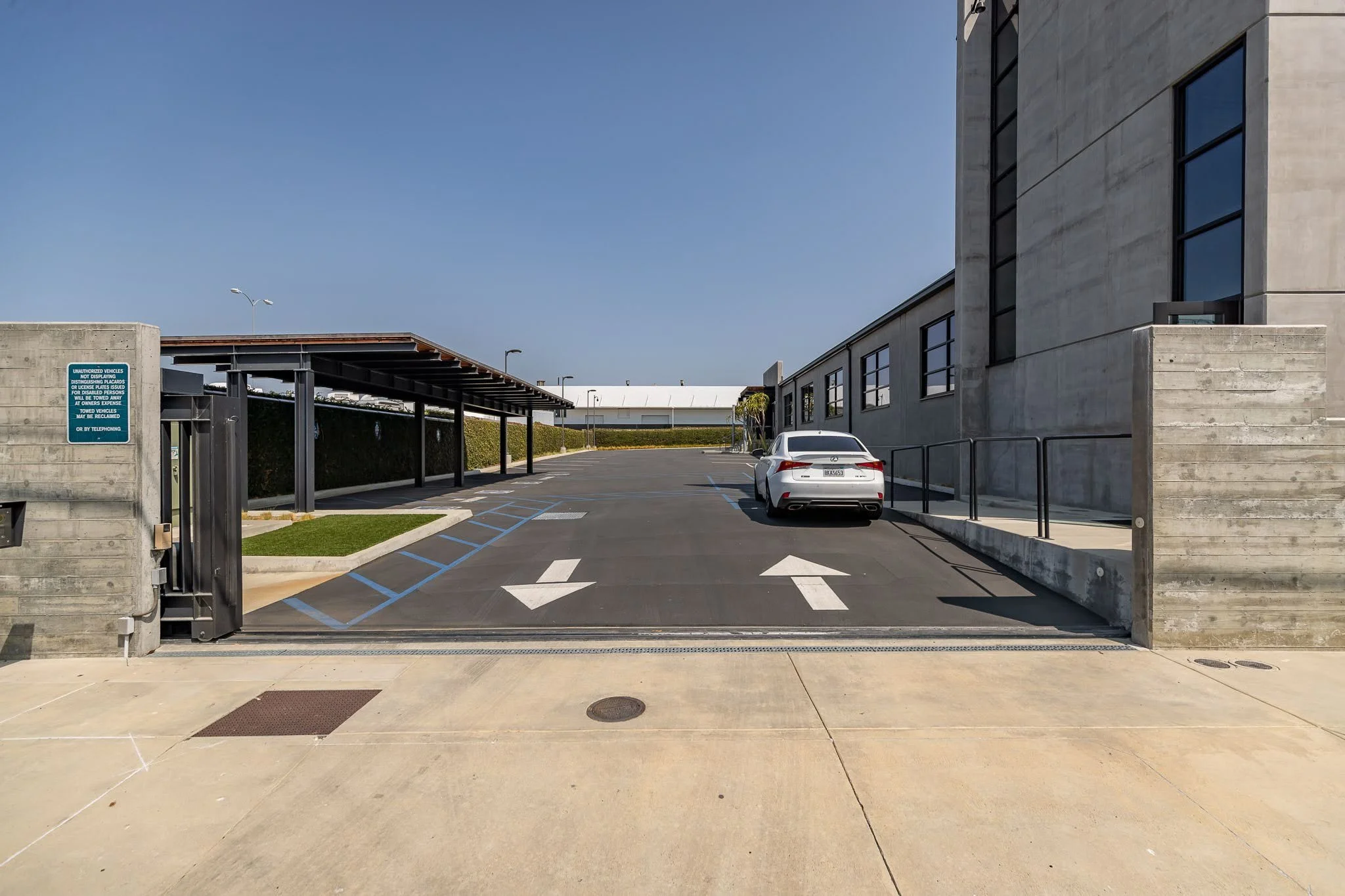 Empty parking lot with a white car parked near a modern concrete building, including designated parking spaces, directional arrows, and a covered bike rack area.