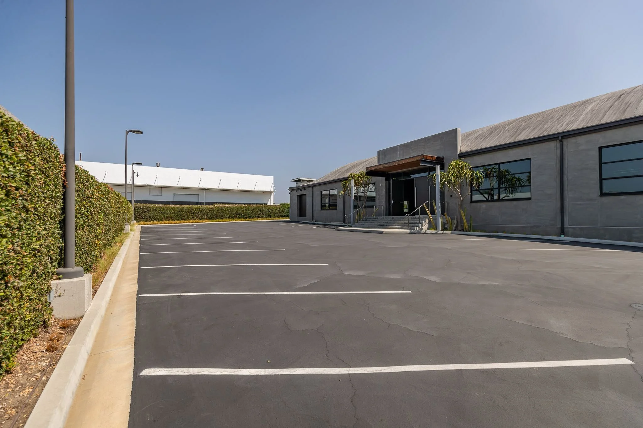 Empty parking lot in front of a modern commercial building under a clear blue sky.