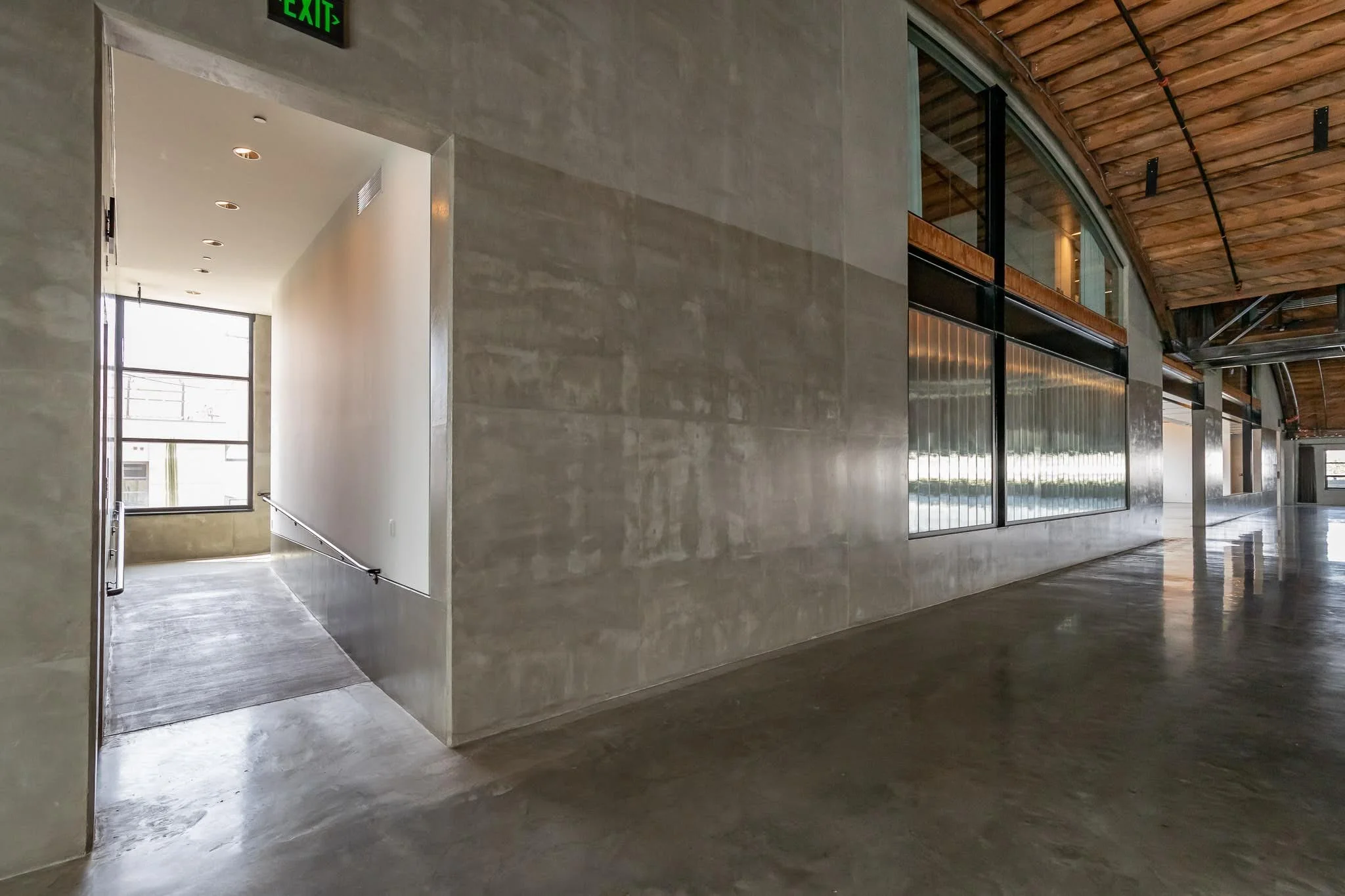 Empty modern interior space with polished concrete floors, large windows, and wooden ceiling panels.