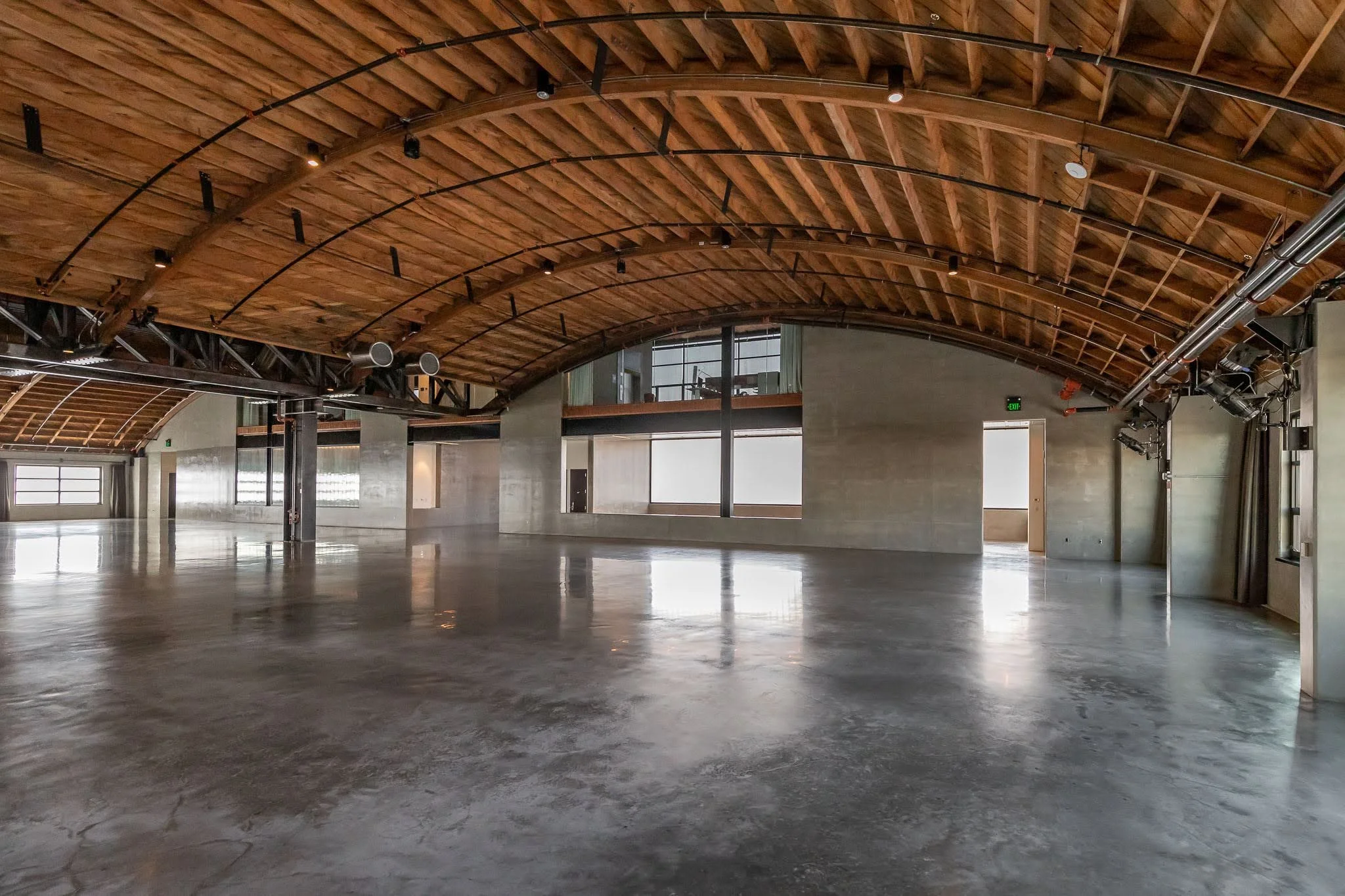 Spacious empty hall with polished concrete floors and a high wooden arched ceiling with track lighting.