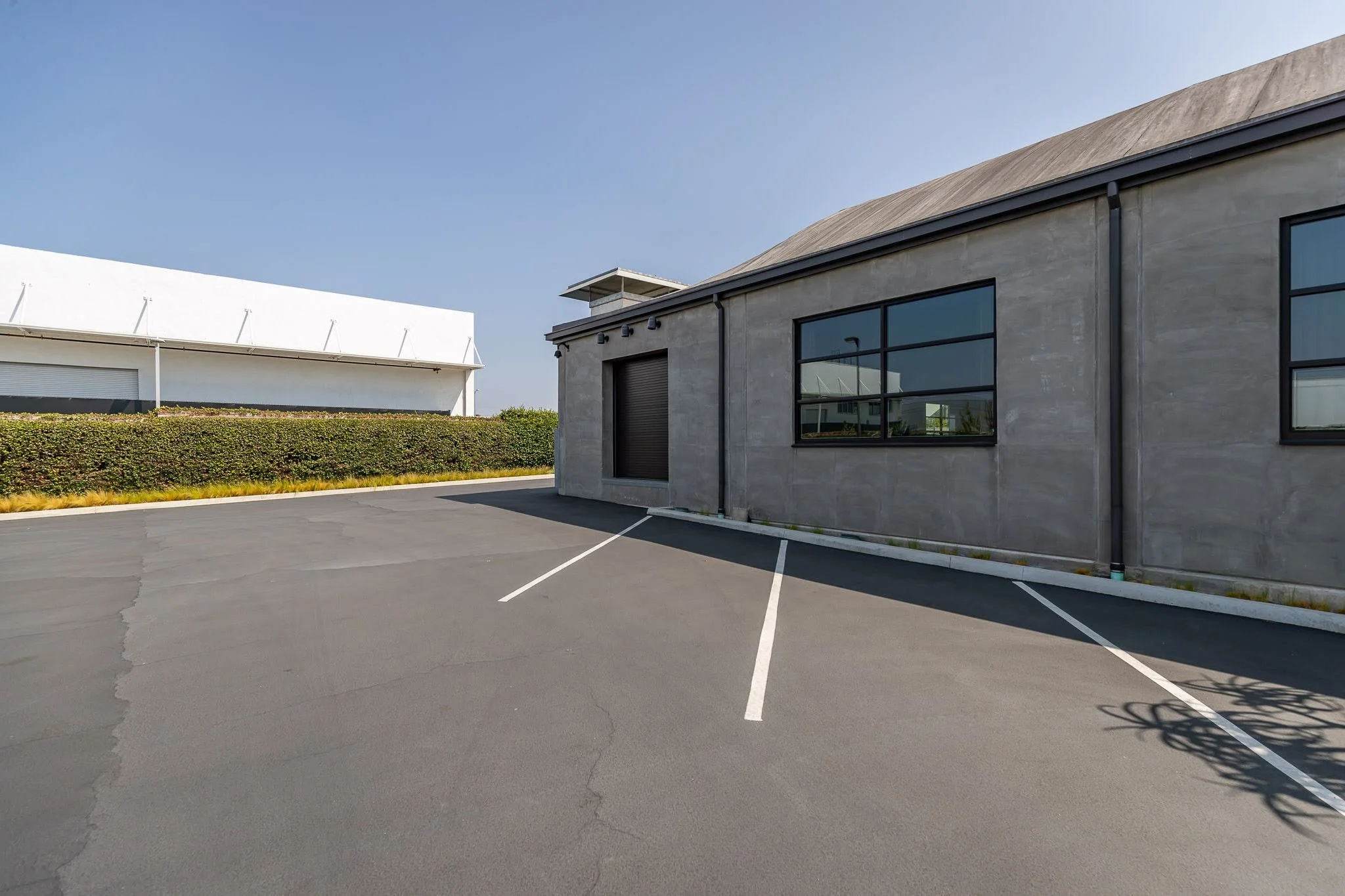 Empty parking lot in front of a modern gray building with large windows on a sunny day.