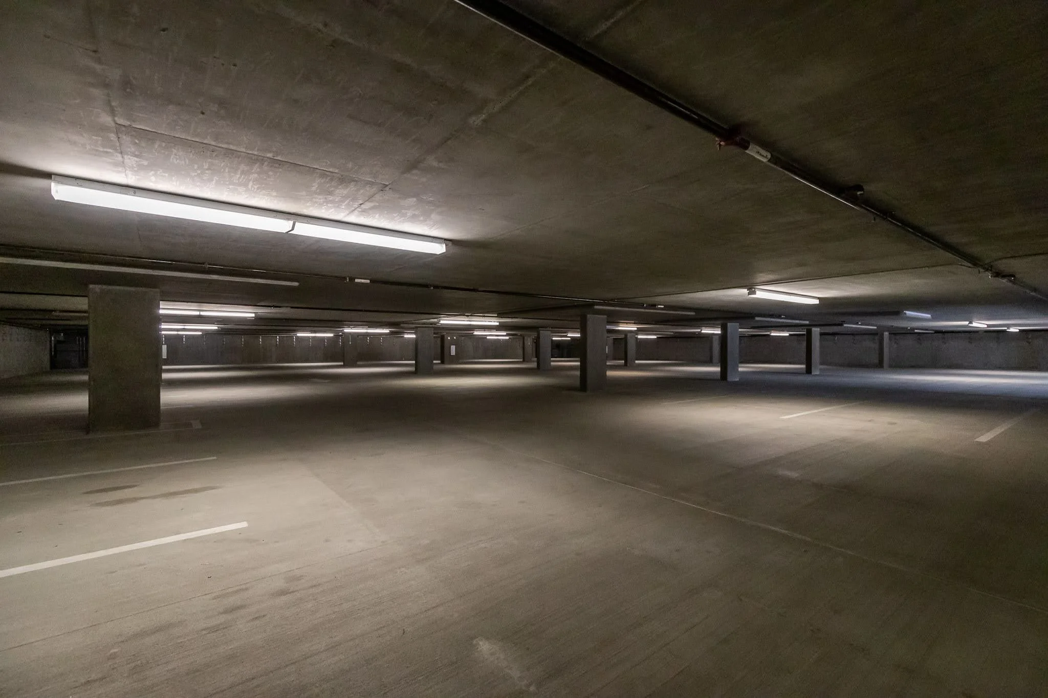 Empty underground parking garage with concrete pillars and fluorescent lights on the ceiling.