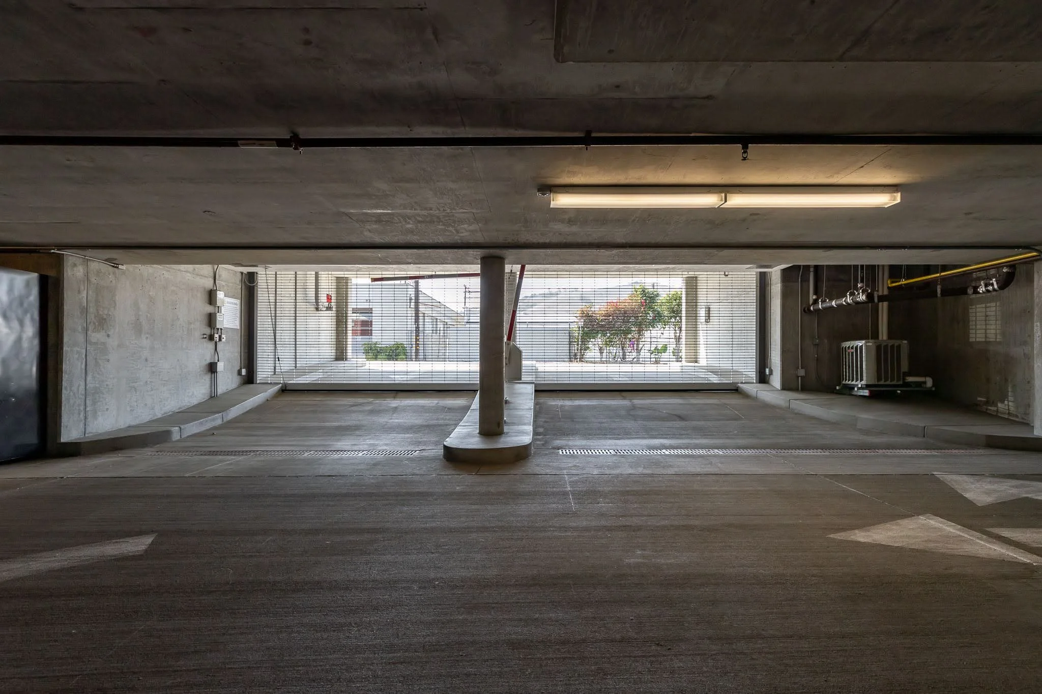 Underground parking garage looking toward the exit with view of street and plants through mesh gate at front.