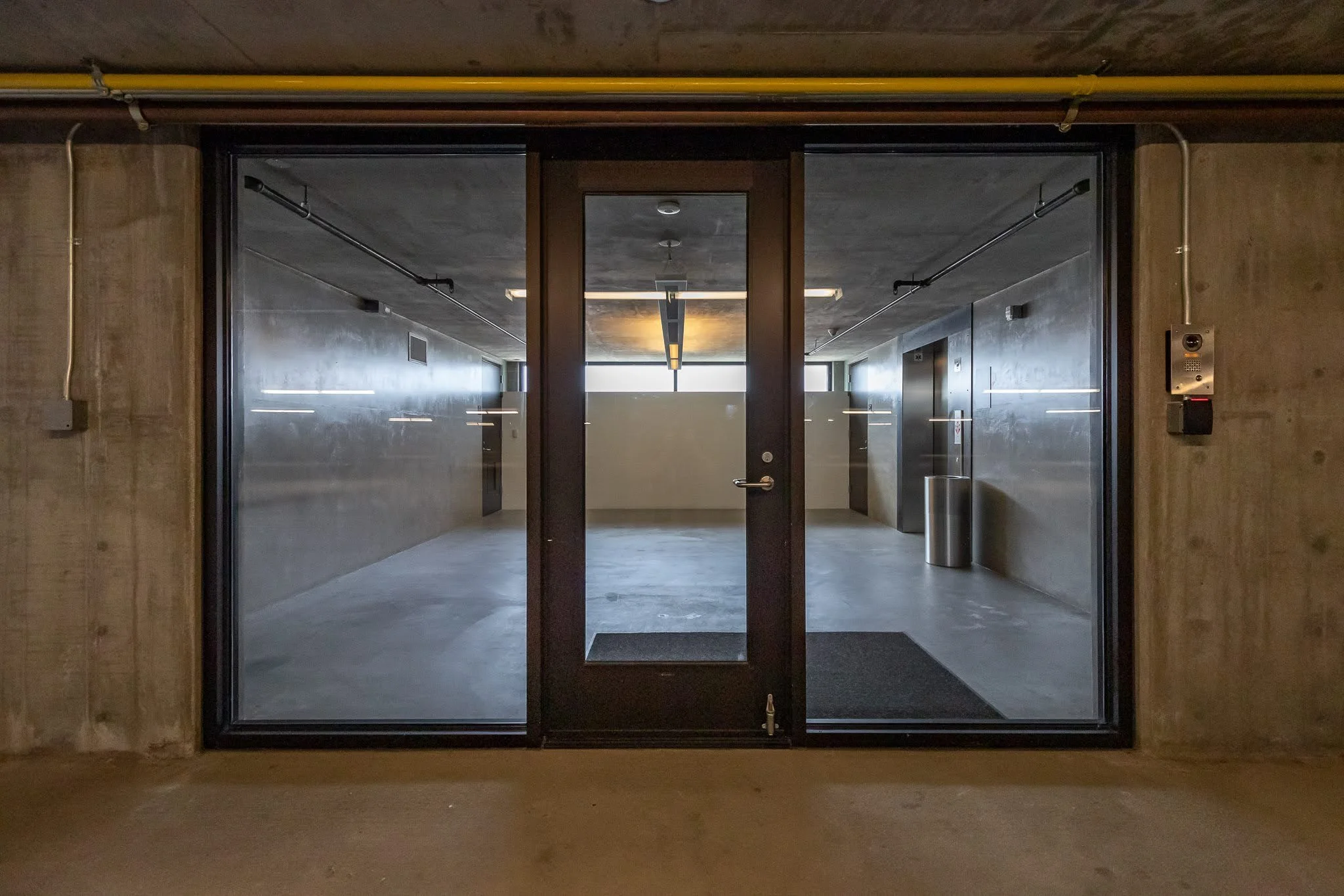 Empty modern hallway with glass doors, concrete walls, and minimal lighting.
