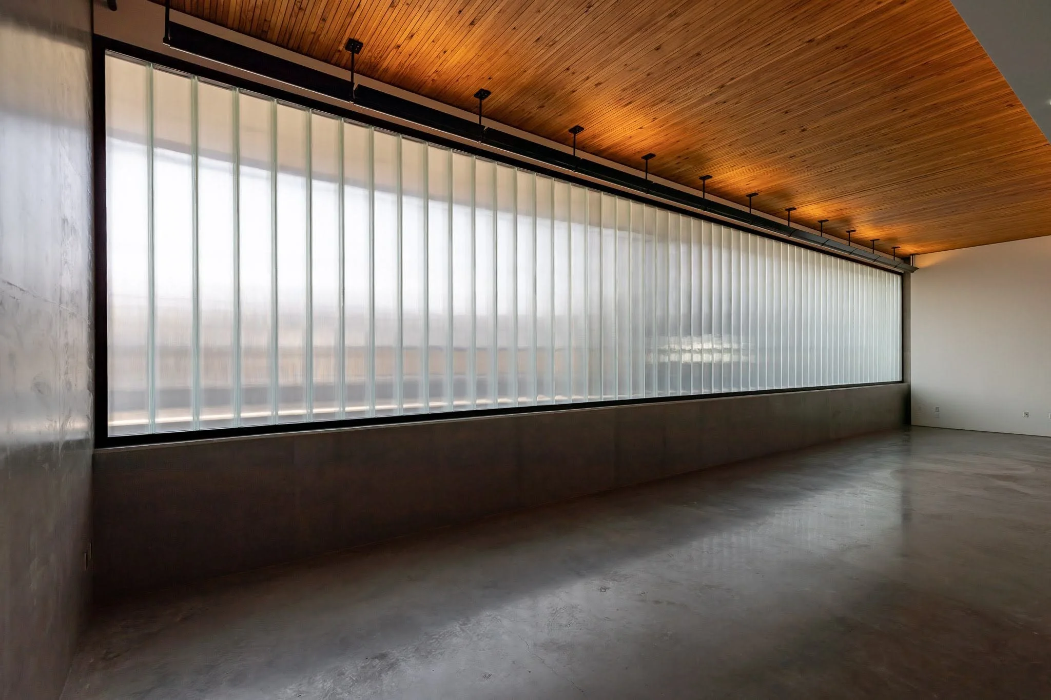 Empty room with a large frosted glass window, concrete floor, wooden ceiling, and white walls.