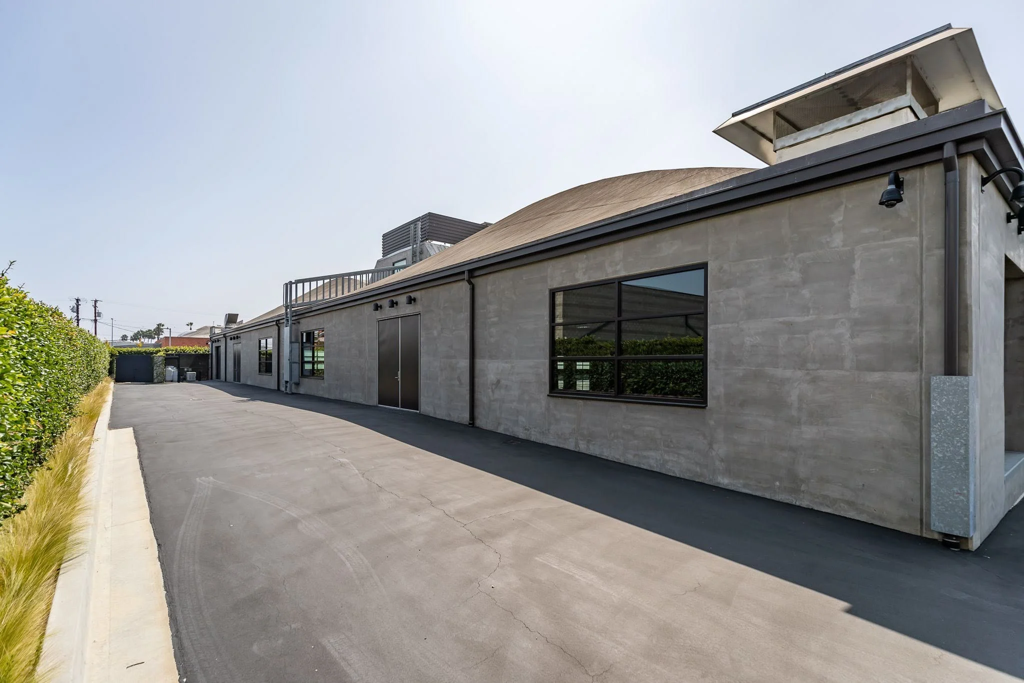 Modern industrial building with gray concrete walls, black-framed windows, and a paved driveway