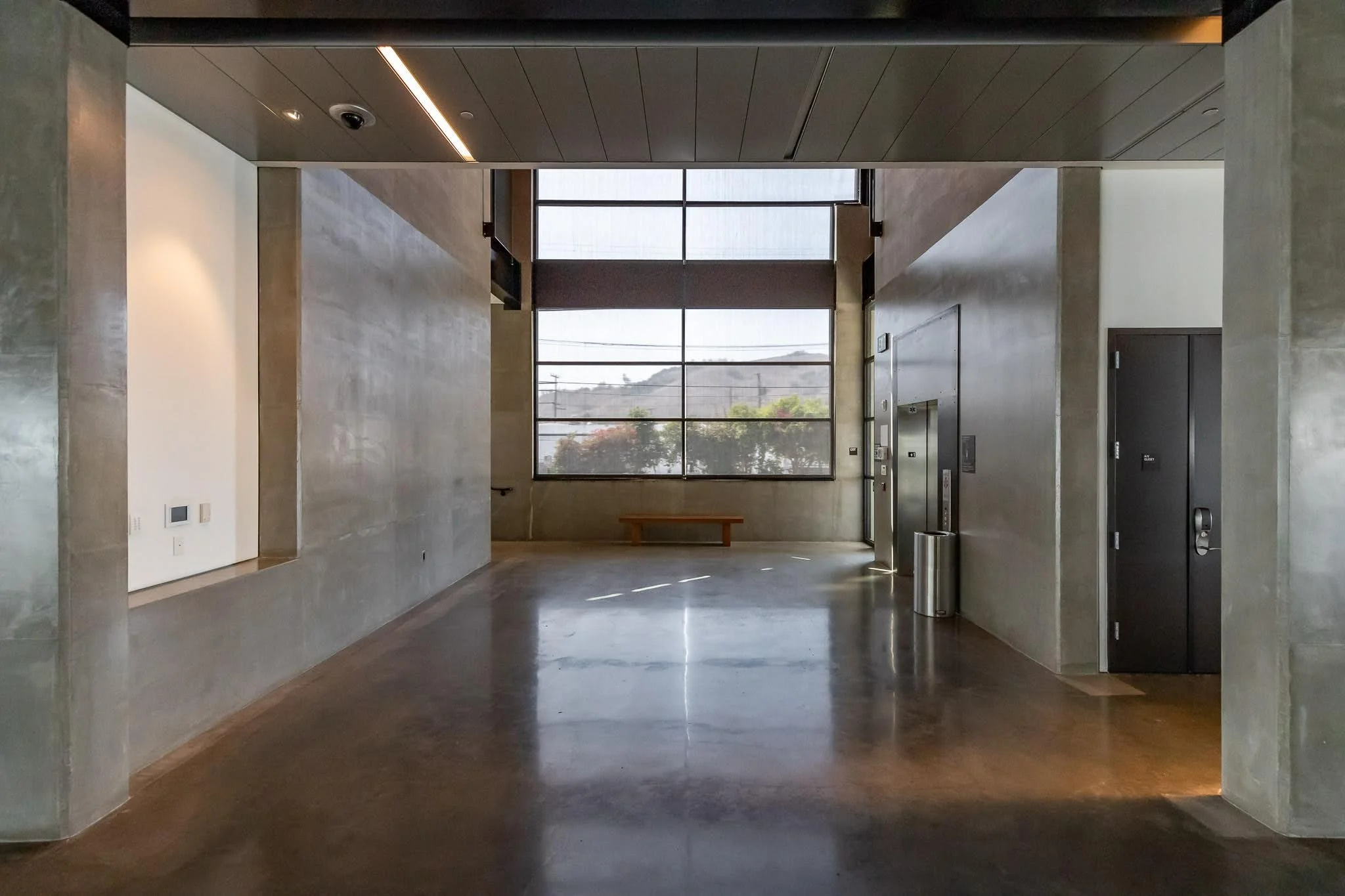 Modern building lobby with large window, bench, elevator, elevator controls, and trash can.