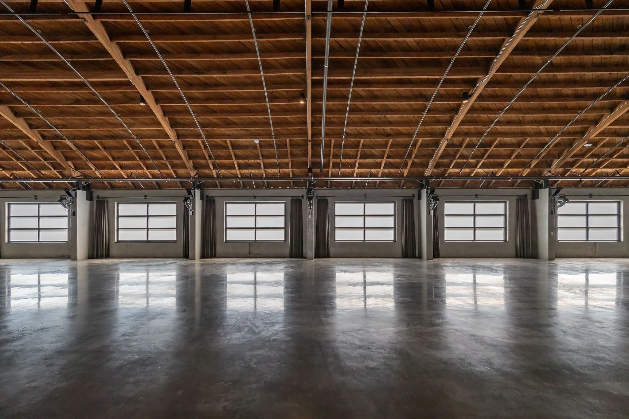 Empty industrial-style warehouse with a polished concrete floor, large windows, and a wooden ceiling with exposed beams.